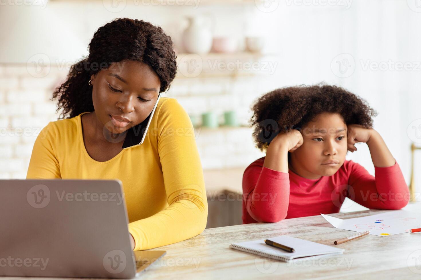 Lack Of Attention. Bored Little Black Girl Sitting Next To Her Busy Mom Working With Laptop And Cellphone In Kitchen, Upset African American Child Feeling Lonely And Depressed, Free Space photo