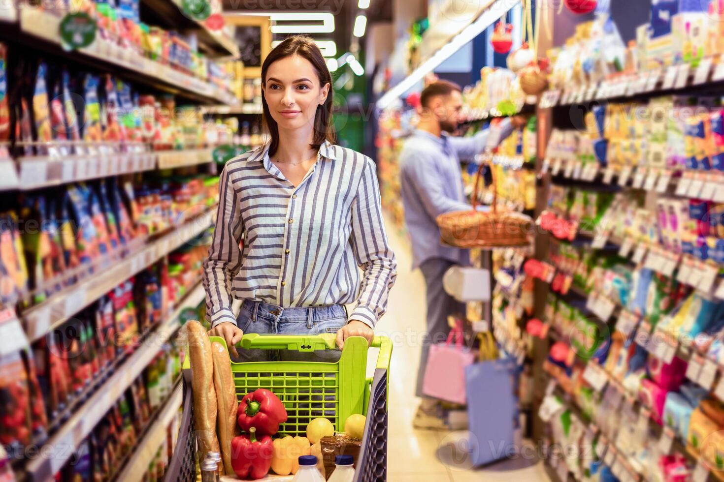 Everyday Shopping. Portrait Of Casual Female Customer Walking With Trolley Cart Between The Aisles In Local Store. Young Woman Buying Healthy Food In Shop, Looking At Shelves, Selective Focus photo