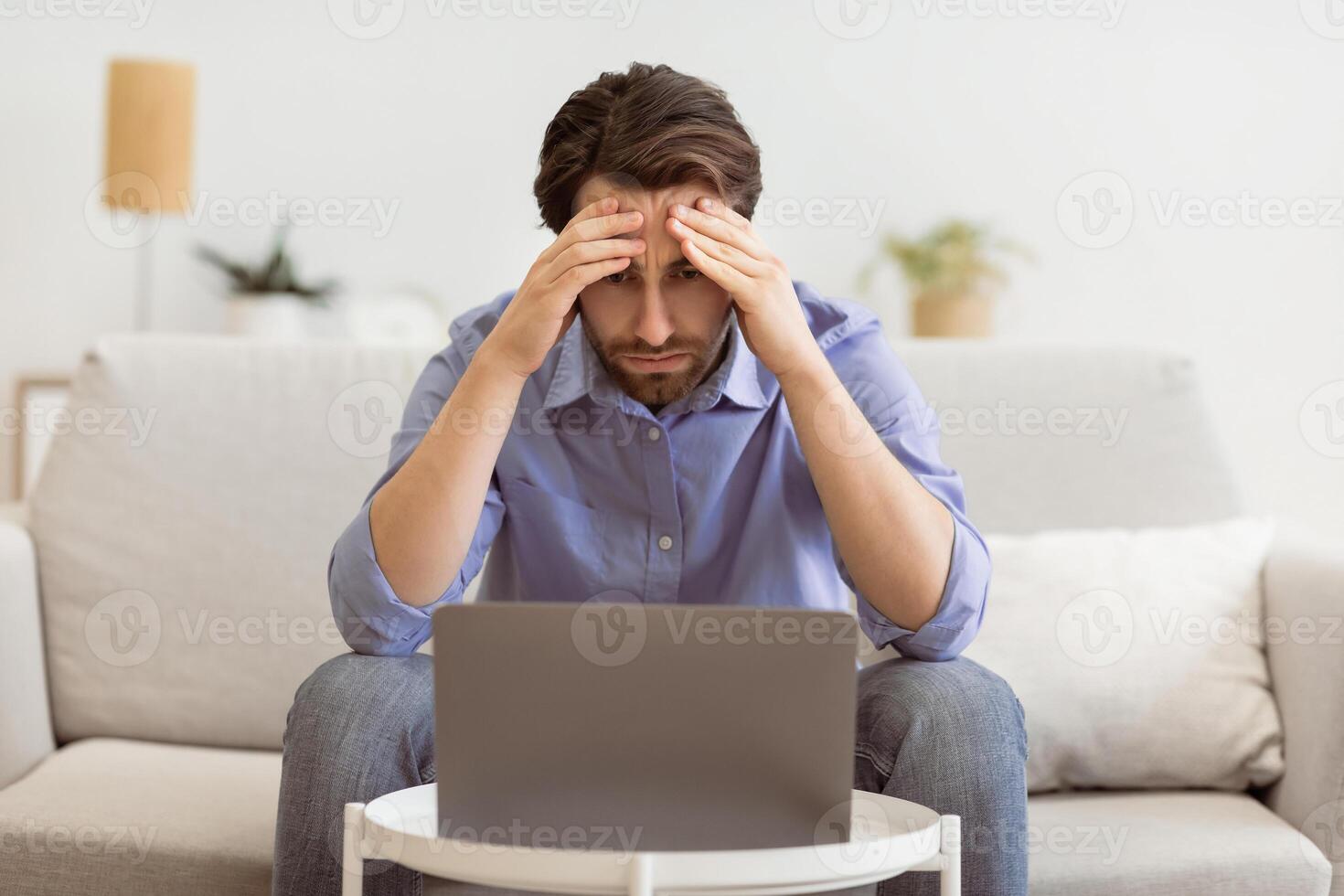 Concerned Businessman At Laptop Touching Head Having Business Problem Sitting On Sofa Indoors. Computer Issue, Unemployment And Remote Work Depression, Business Fail And Bankruptcy Concept photo