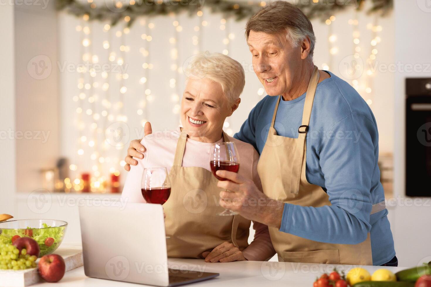 Happy Aged Couple Making Call On Laptop Celebrating Christmas Toasting And Drinking Wine In Kitchen At Home. Xmas And New Year Holidays Celebration During Coronavirus Pandemic Quarantine photo