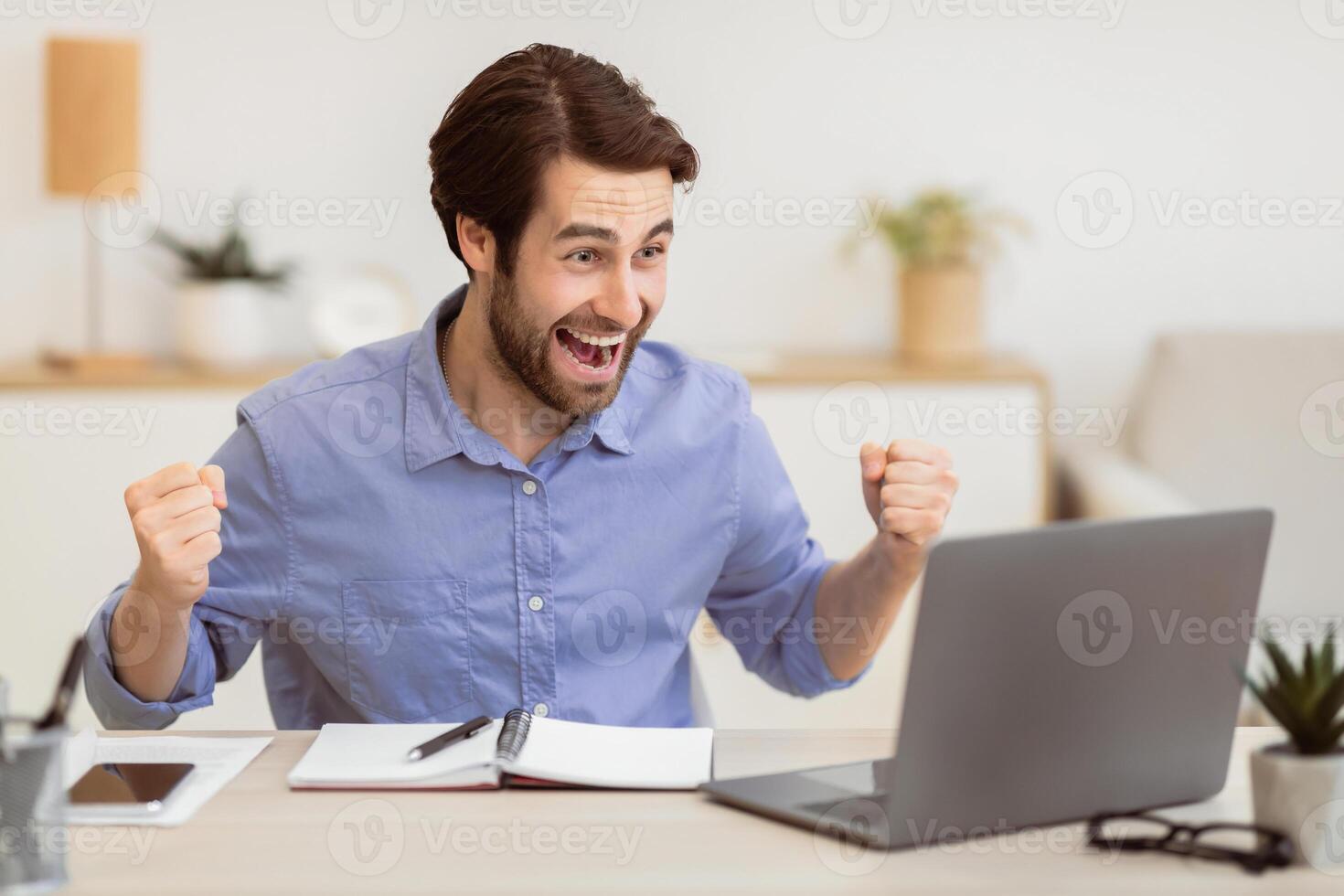 Excited Young Businessman At Laptop Computer Shaking Fists And Shouting Looking At Screen Sitting At Workplace In Modern Office, Celebrating Business Success. Victory Celebration, Successful Career photo
