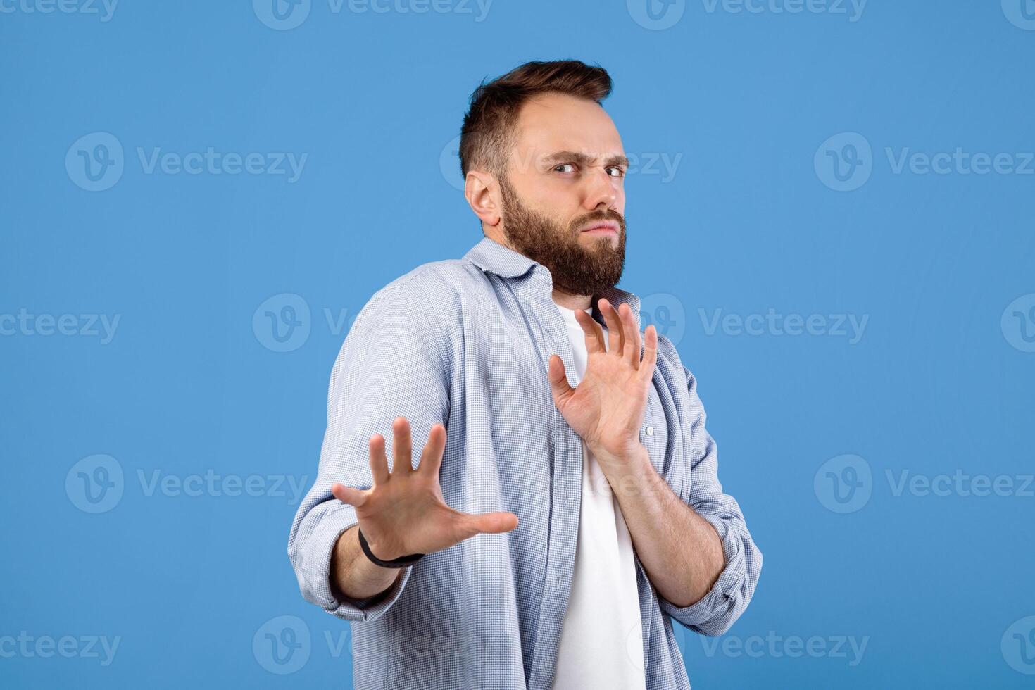 Repulsed millennial guy rejecting something, making STOP gesture over blue studio background. Revolted young man feeling disgusted, expressing rejection or dislike photo