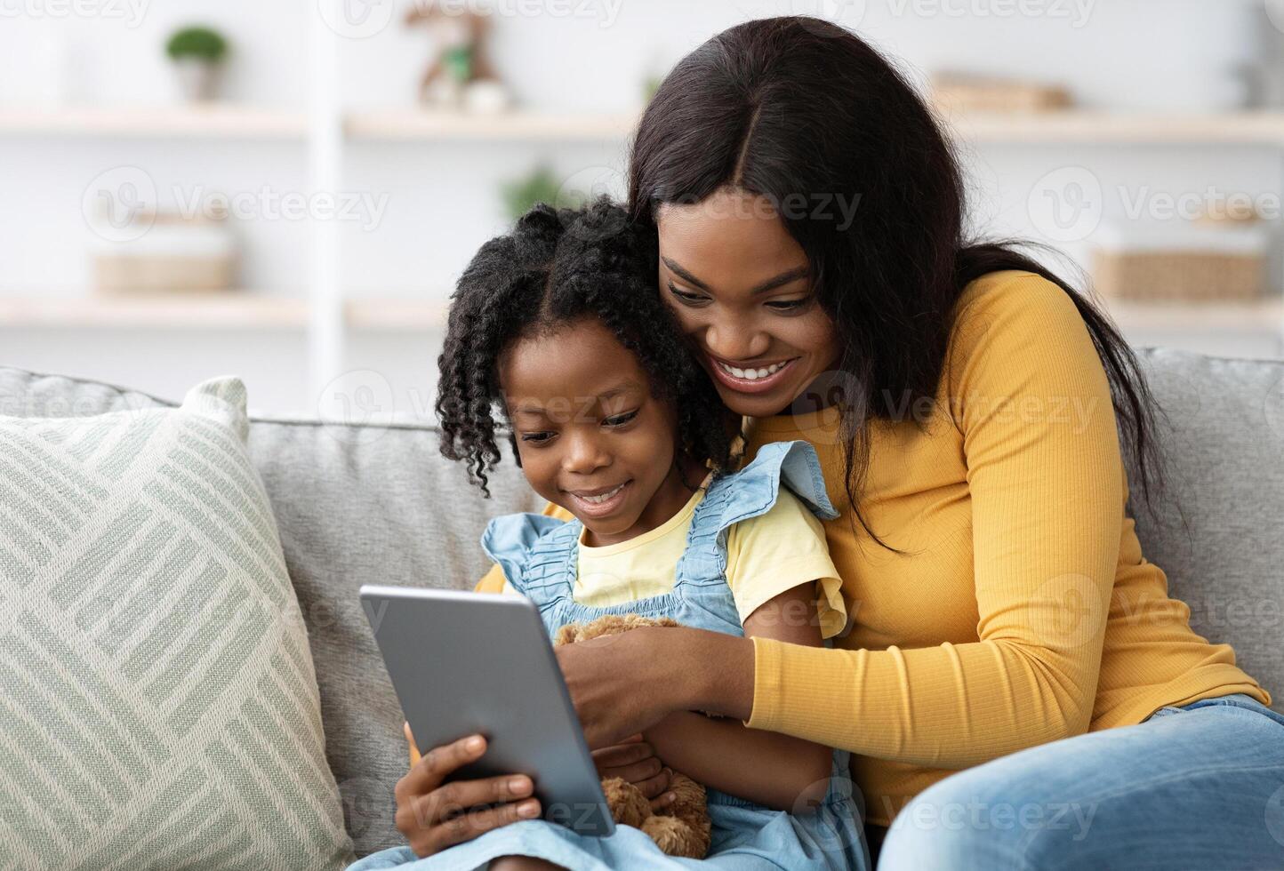 Technologies For Leisure. Happy Black Mother And Little Daughter Using Digital Tablet Together While Sitting On Couch At Home, African American Mom And Female Child Shopping Online With Modern Gadget photo