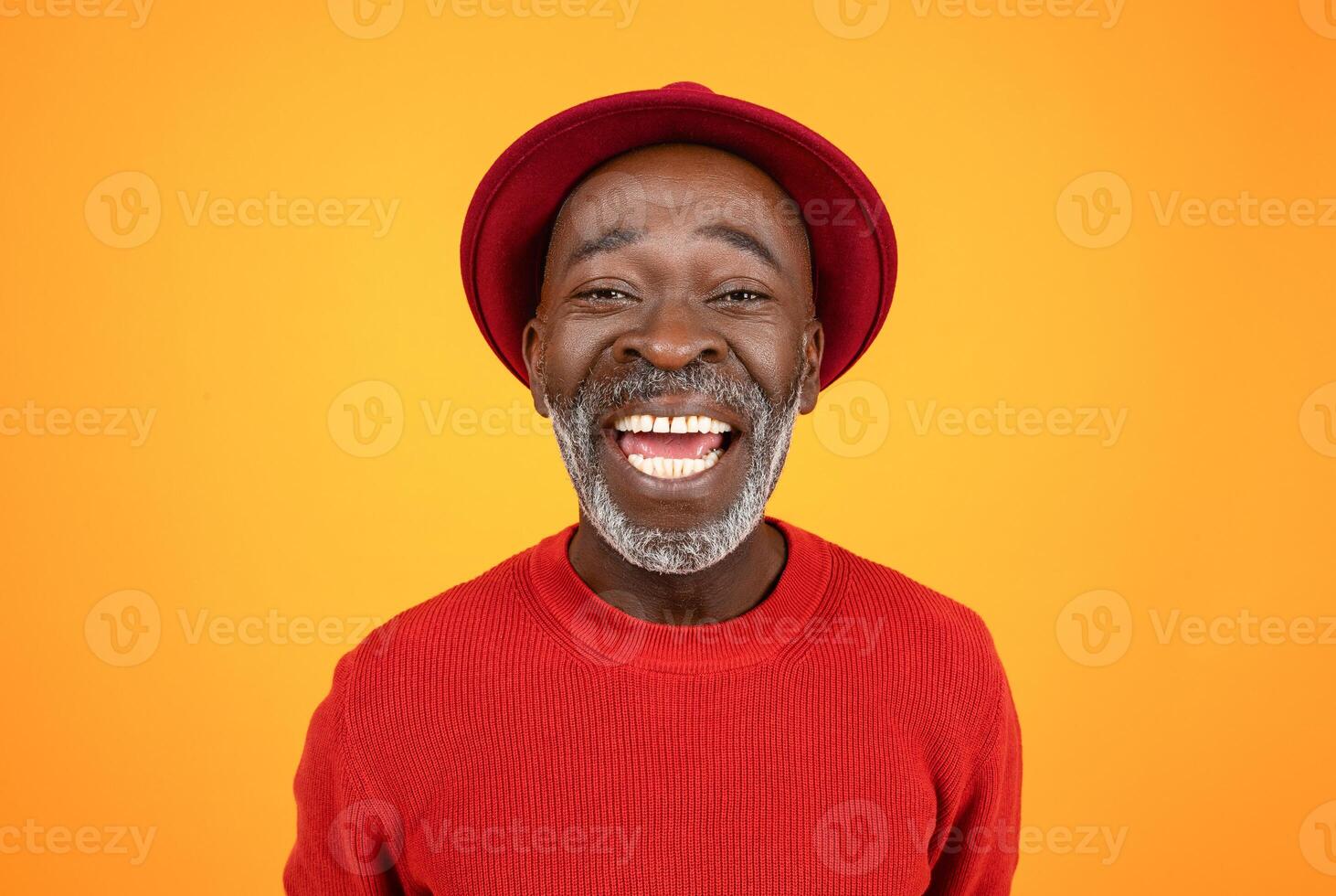 Happy excited senior african american man in hat and red clothes, with open mouth, look at camera, isolated on orange studio background, close up. Portrait, headshot for call photo