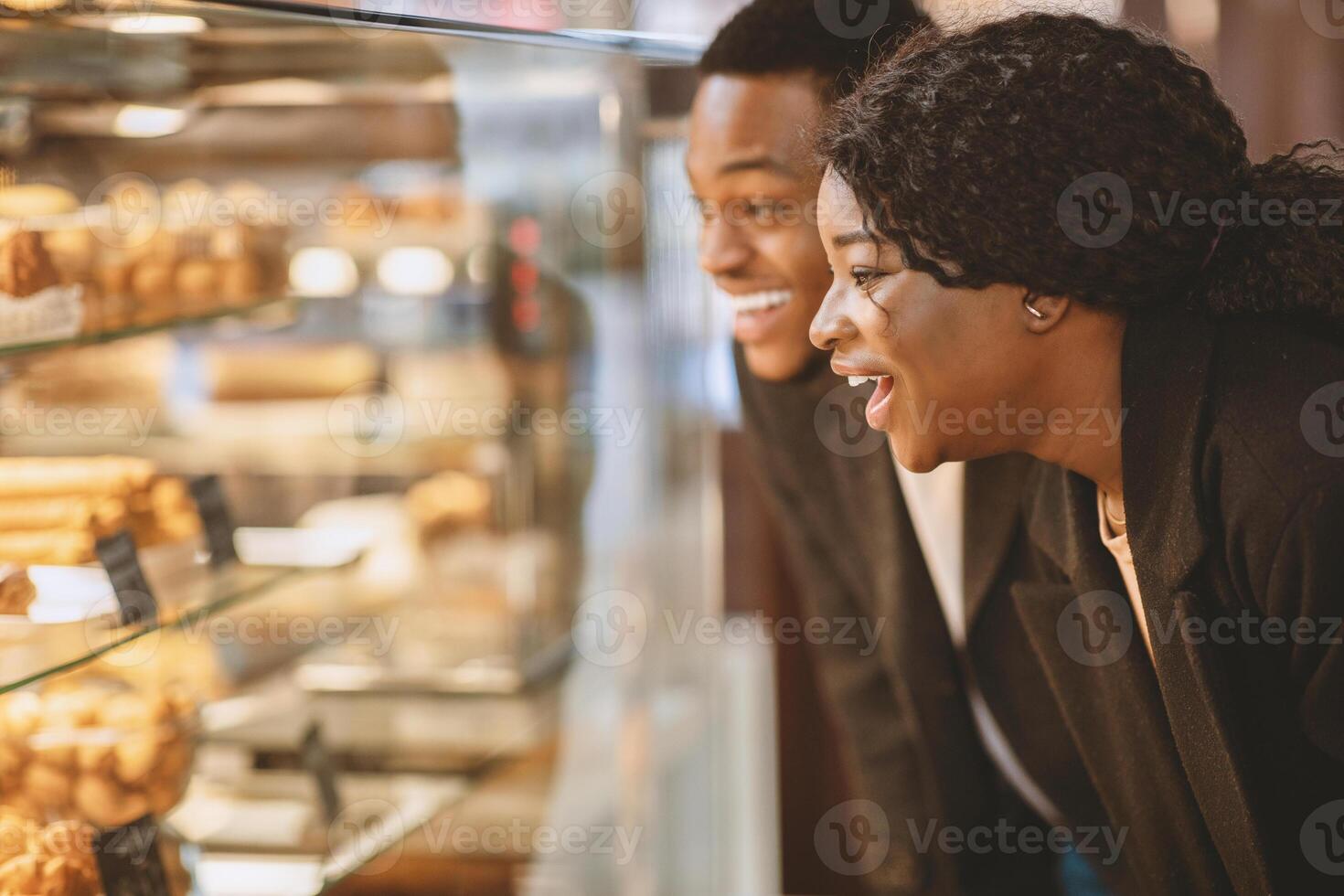 Couple together choosing sweets. Surprised happy millennial woman and man standing in front of glass showcase with pastries and cakes in modern grocery store, side view, close up, free space photo