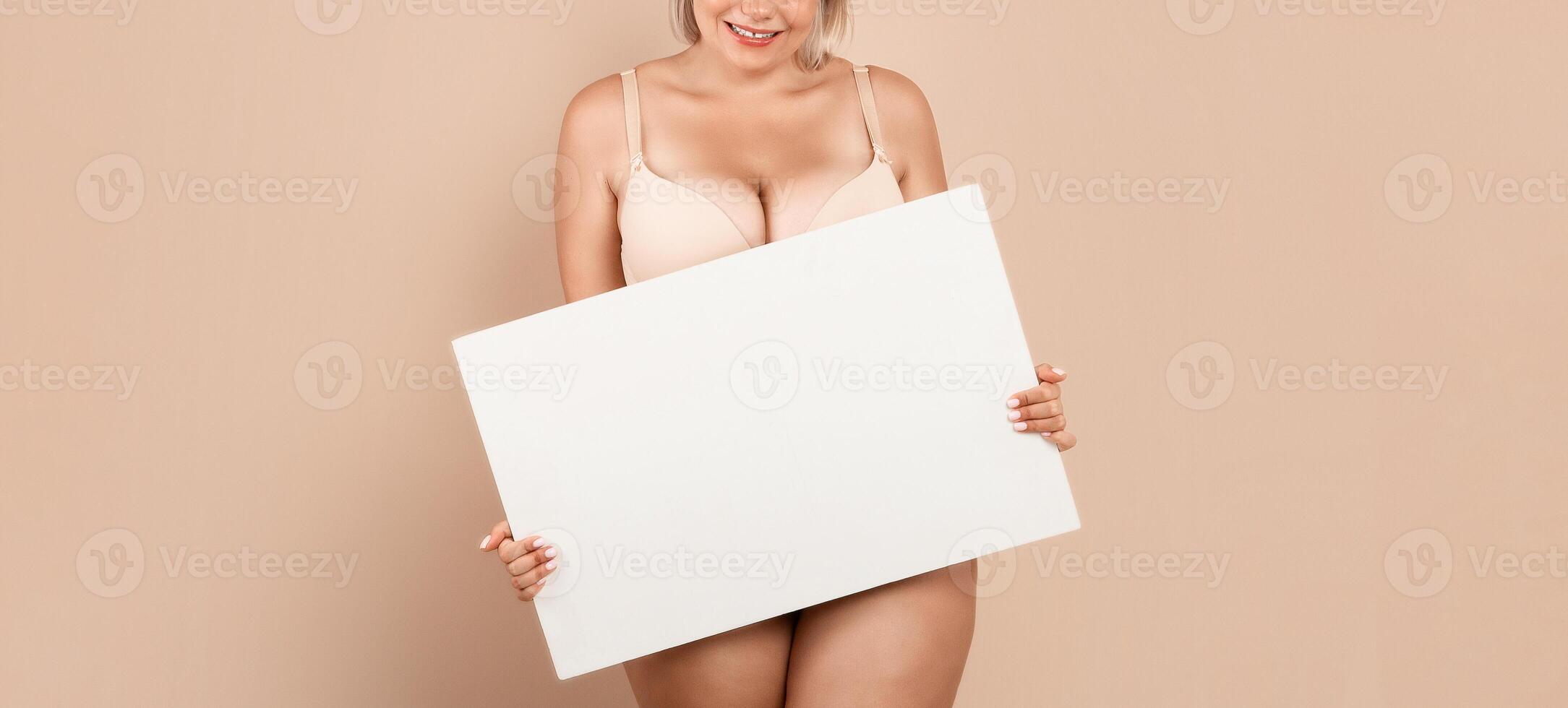 Cheerful Plus Size Female In Underwear Holding White Blank Placard With Copy Space For Advertisement Or Motivational Inscription, Positive Curvy Lady Posing In Lingerie Over Beige Studio Background photo