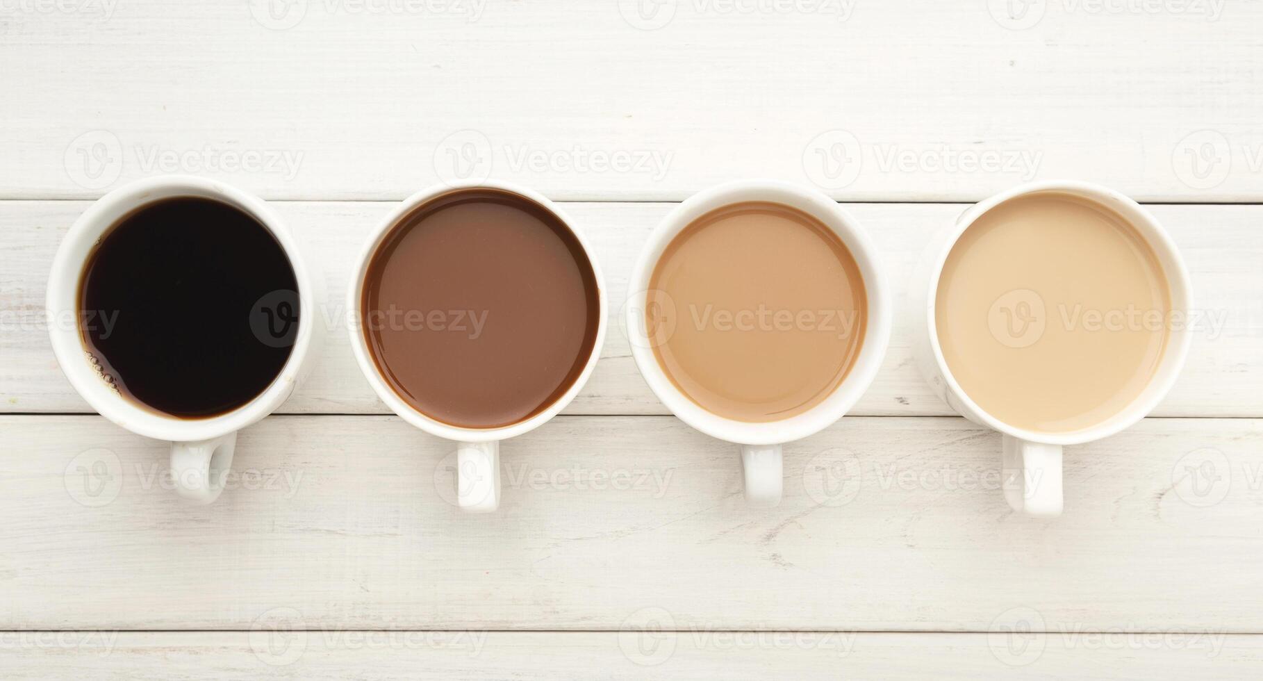 Different cups of coffee on white wooden table, top view. Gradient from light americano with milk to strong black espresso, copy space photo