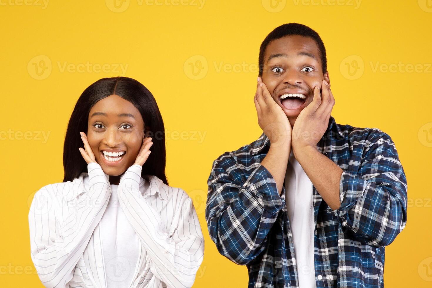Happy, funny and surprise are natural emotions. Amazed african american young man and woman with open mouths seeing something unusual and very glad, isolated on yellow background, studio shot photo