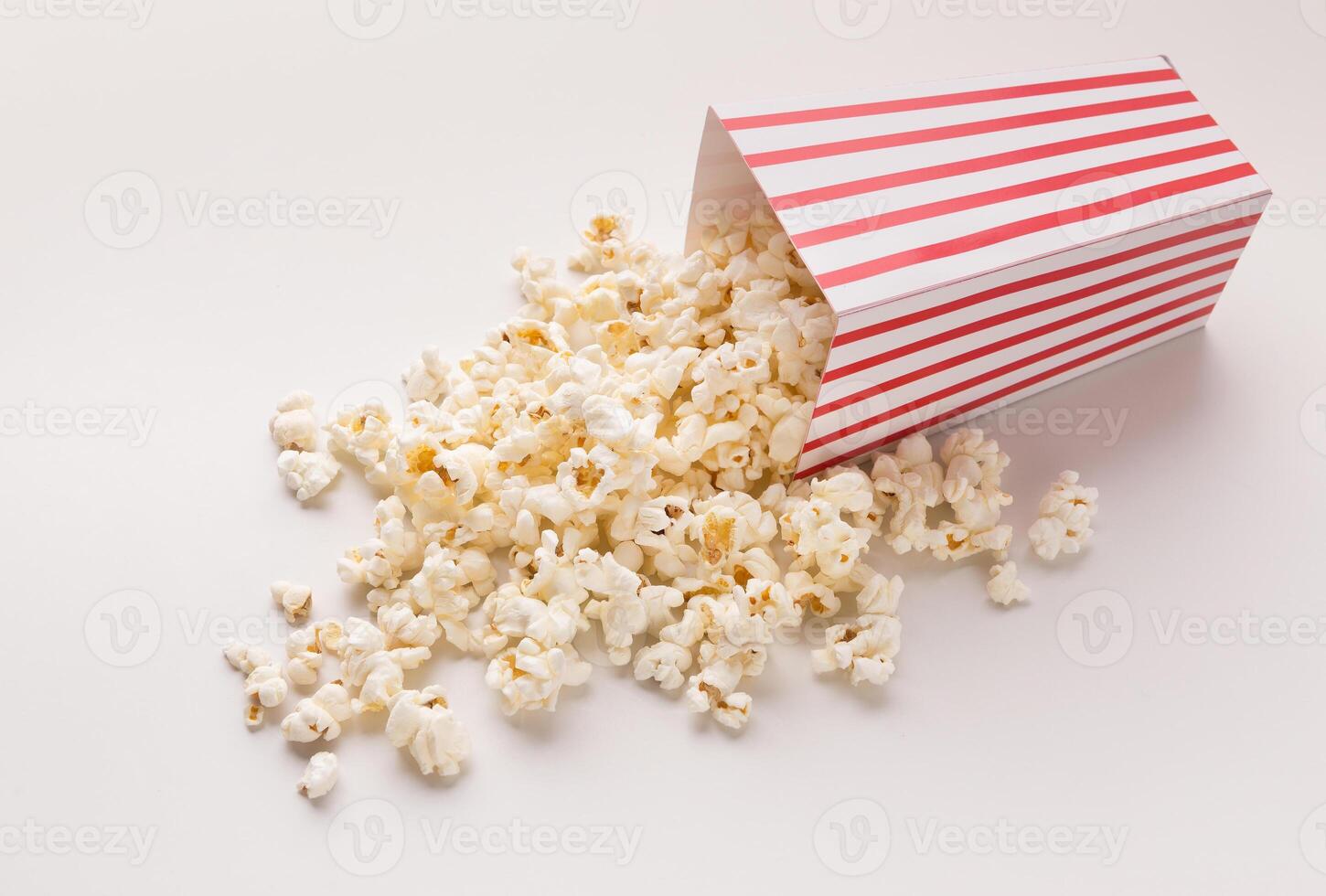 Popcorn in classic striped bukcet on white background. Hot corn scattered from paper box, copy space. Fast food and movie snack photo