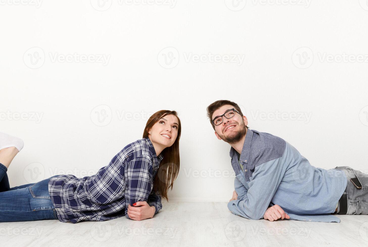 Dreamy couple lying on floor in empty room and looking up, imagine future interior design project, white background photo