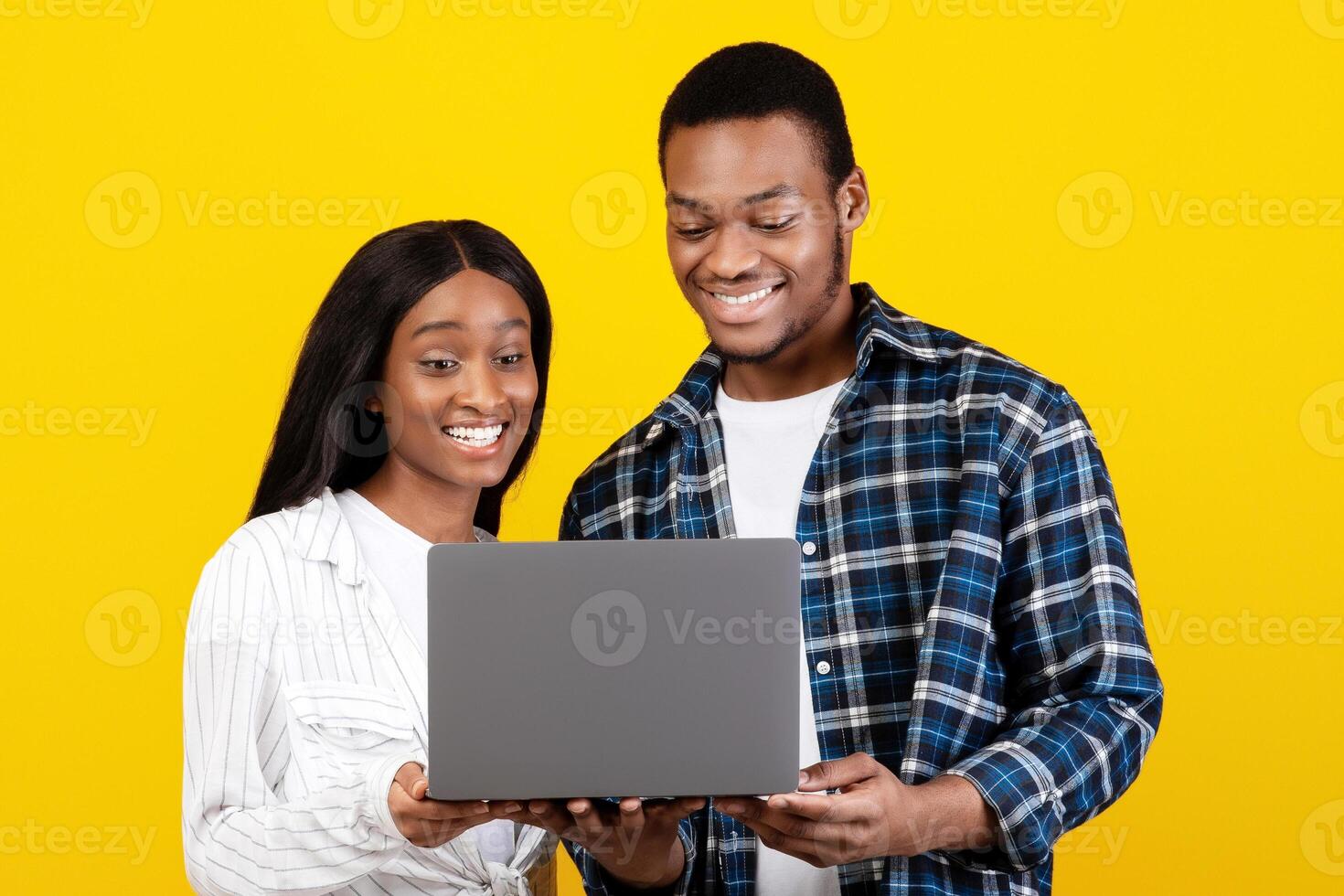 Online education, remote work and shopping. Happy millennial african american couple looking at laptop and choosing purchase or watch lesson or , isolated on yellow background, studio shot photo