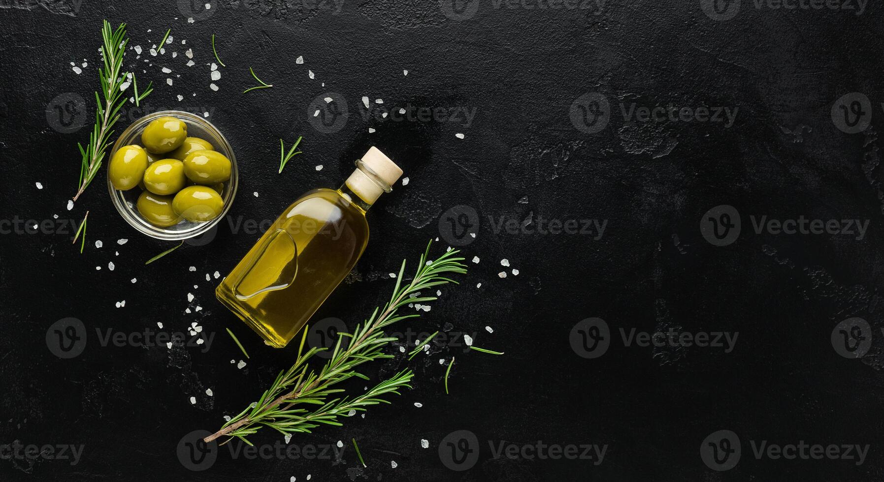 Olive oil, fresh olives and rosemary sprigs on black background, top view, copy space. Organic olive oil concept photo