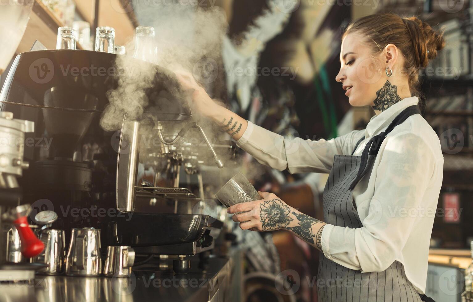 Happy young tattooed barista making coffee in professional coffee machine. Woman preparing beverage. Small business and professional coffee brewing concept photo