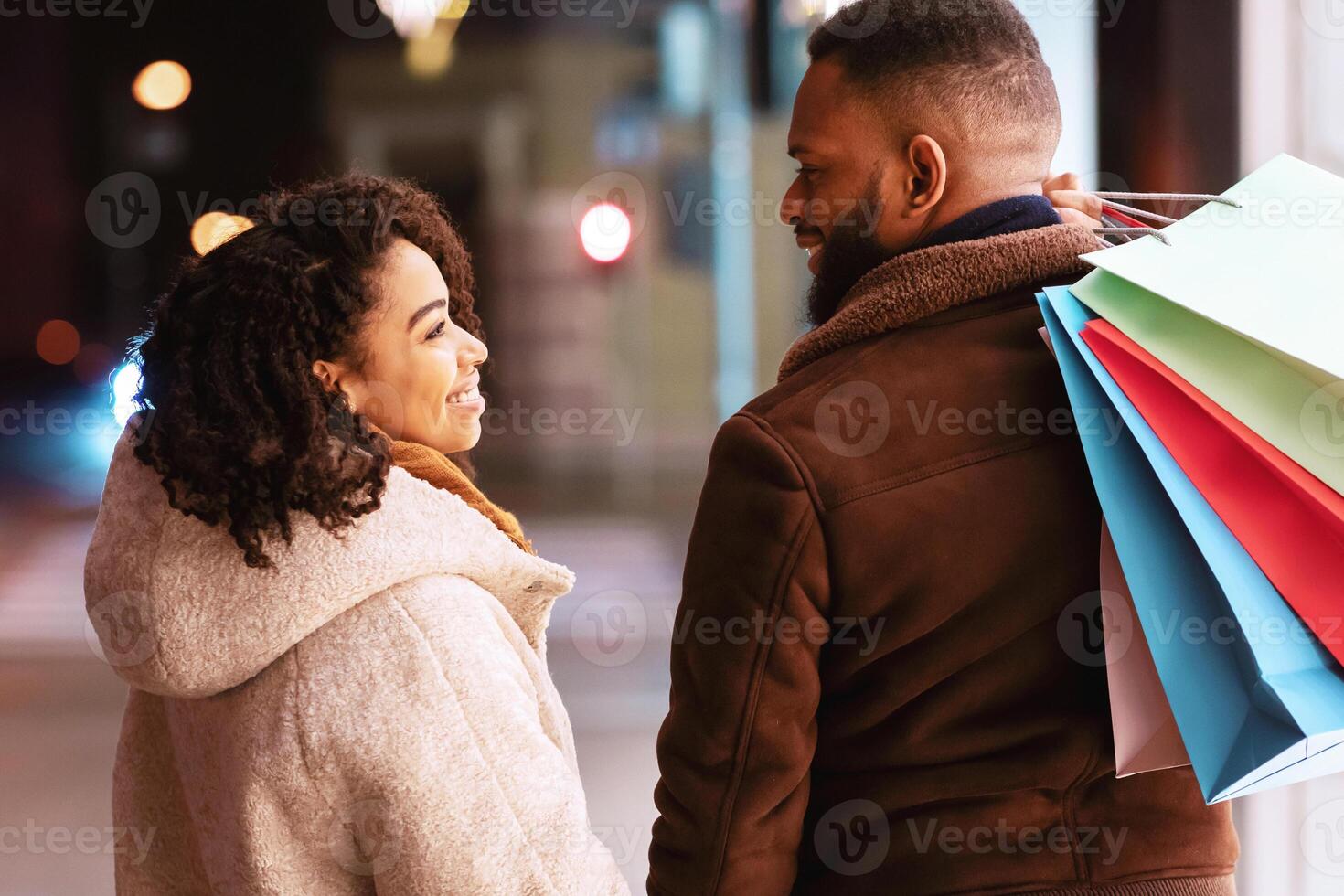 Happy Loving Family. Back rear view portrait of smiling african american man and woman looking at each other, carrying shopping bags and holding hands while walking near mall in the evening photo