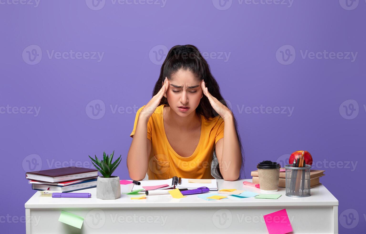 Portrait of fatigue tired indian lady feeling headache or stress, touching and massaging her temples, trying to learn and study, sitting at desk with notebook. Woman doing homework and thinking photo
