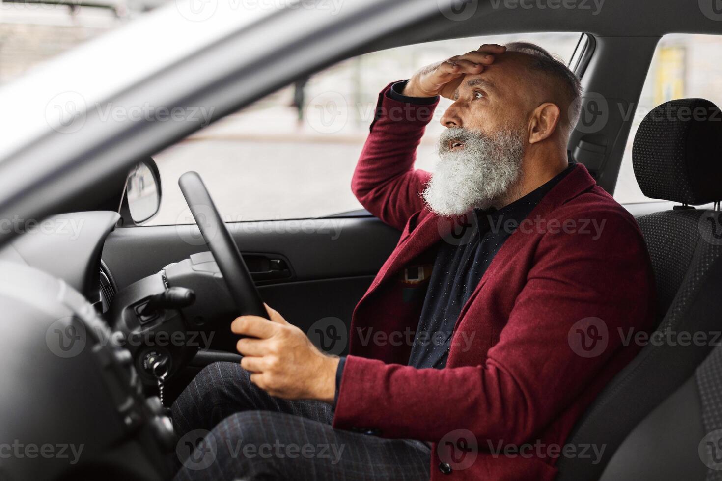 Shocked senior businessman having troubles on road, sitting in car, touching his head, side view, copy space. Astonished grey-haired aged man having car accident, suffering from stress photo