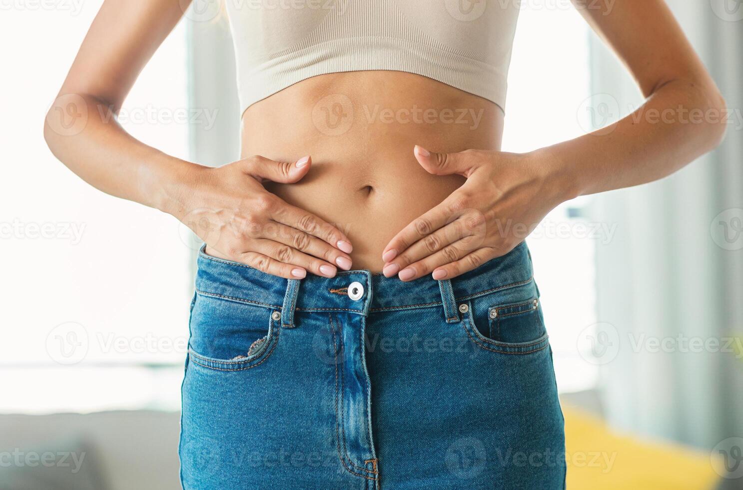 Weight Loss. Unrecognizable Slim Lady Touching Flat Stomach Framing Belly Button With Hands Posing Standing At Home. Slimming And Abdomen Health Concept. Cropped Shot photo