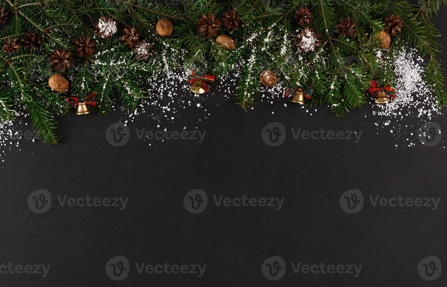 Christmas background with copy space, top view on pine tree twigs with pine cones, nuts and snow frame on black table. Xmas decorations, winter holidays concept photo