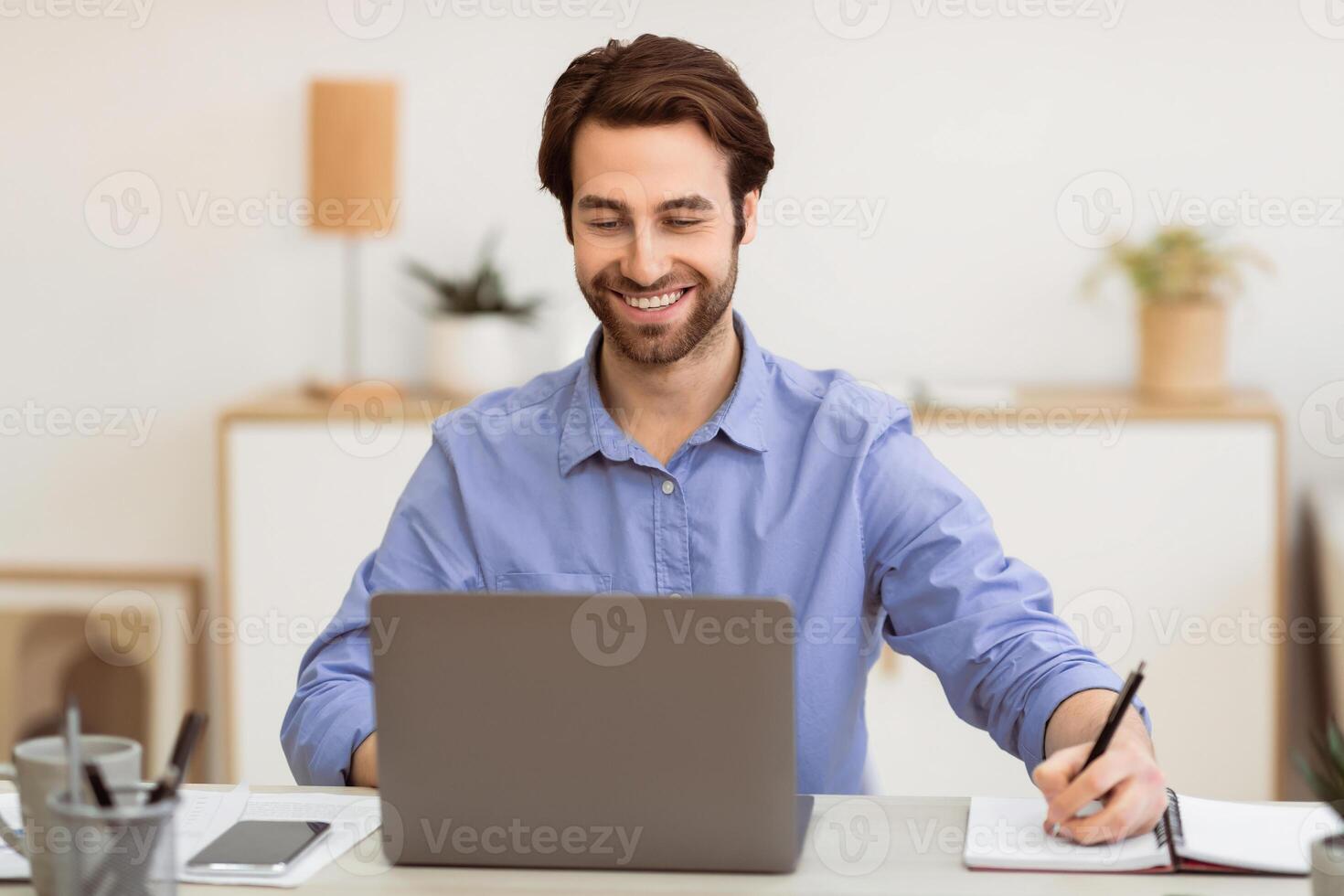 Cheerful Businessman Writing Taking Notes Working On Laptop Sitting At Workplace In Modern Office. Successful Business Career, Entrepreneurship Concept. Selective Focus photo