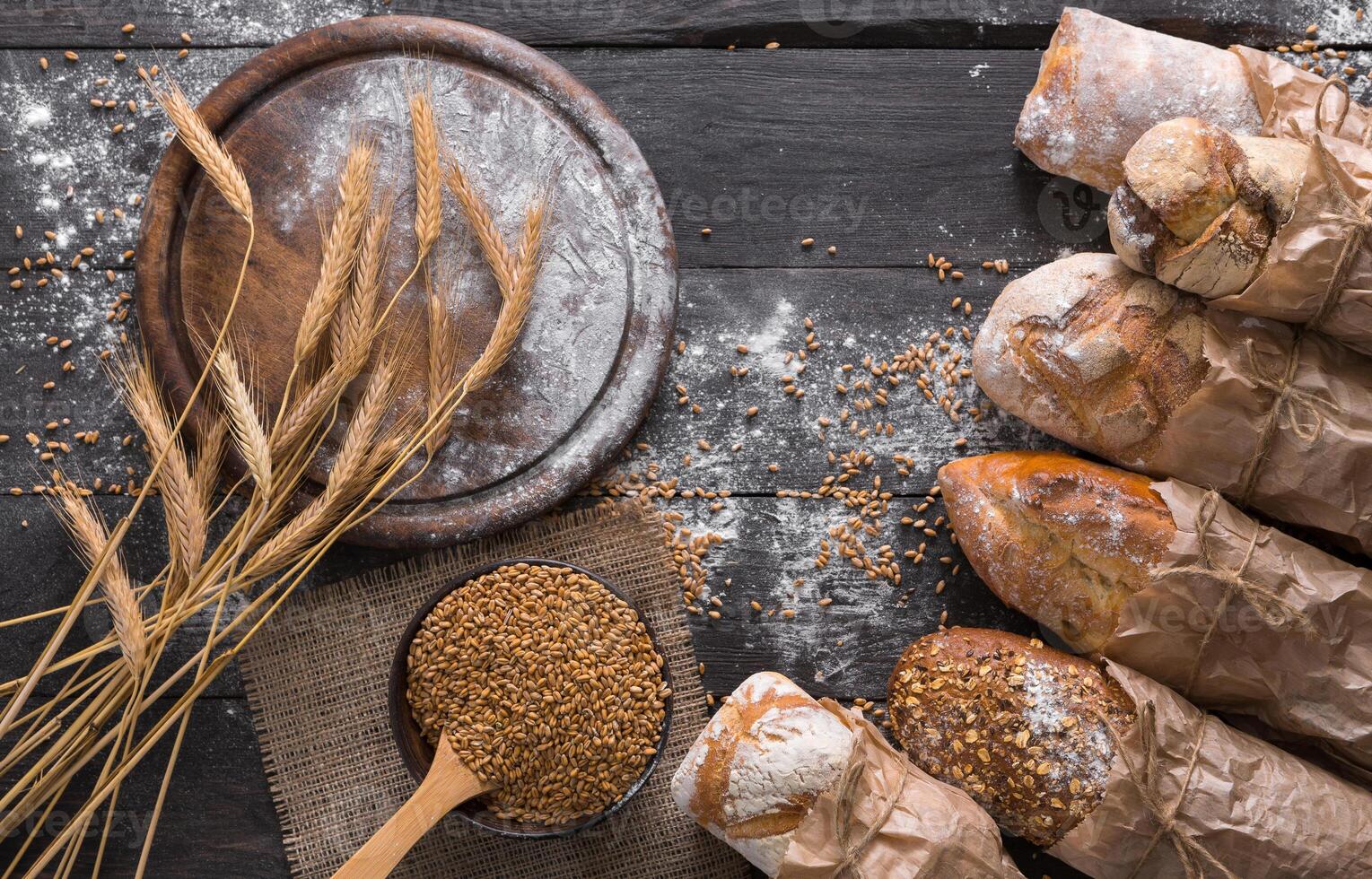Bread background. Brown and white whole grain loaves wrapped in kraft paper composition on rustic dark wood with empty desk copy space. Baking and home bread making concept. Soft toning photo