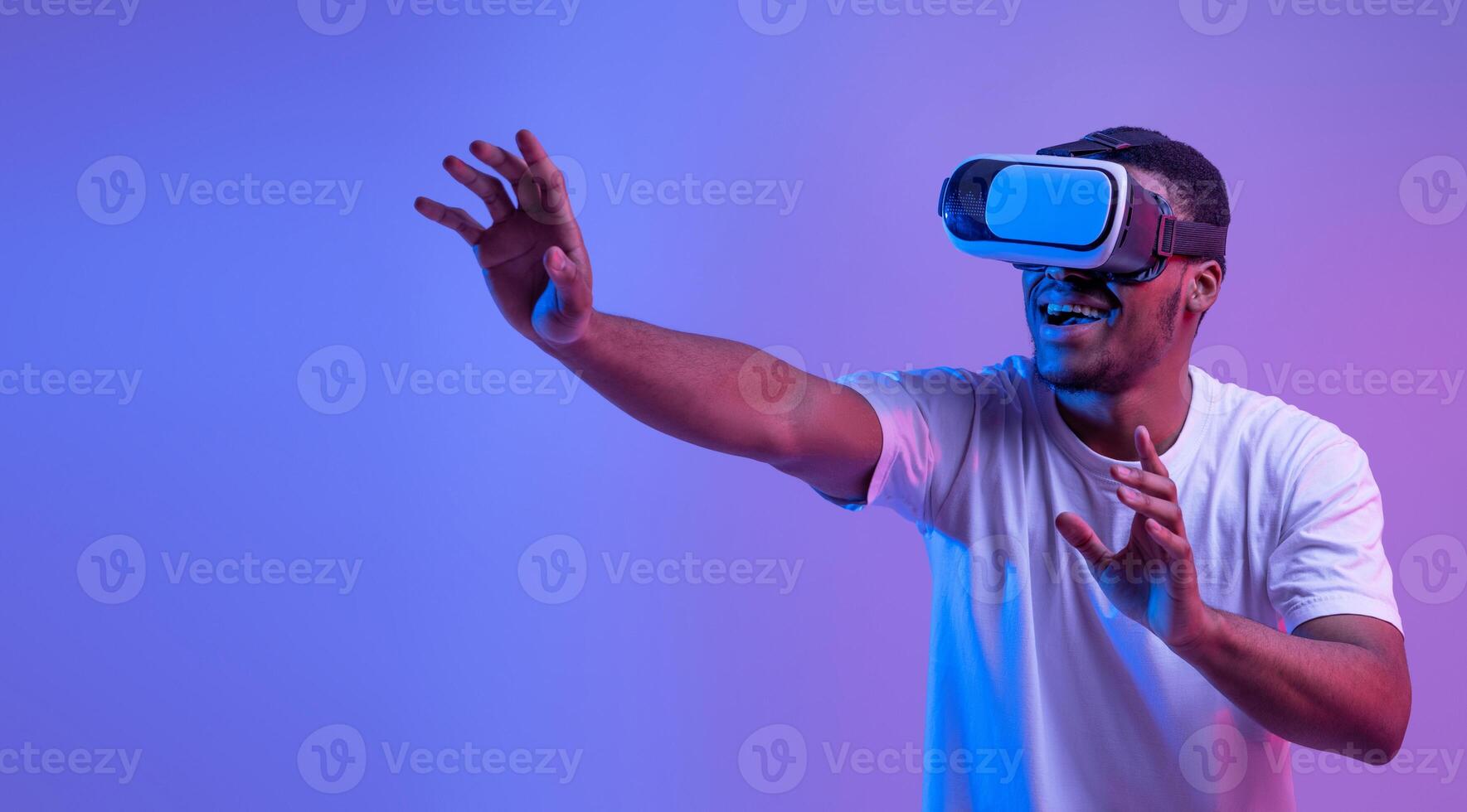 Virtual Experience. Excited African American Man In neon Lighting Wearing VR Headset, Touching Air While Playing Game, Amazed Black Guy Standing Over Purple Background, Panorama With Copy Space photo