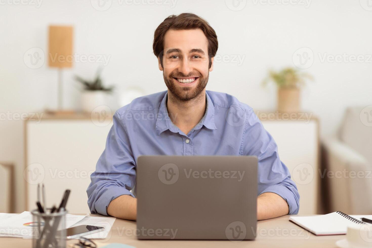 Successful Businessman Sitting At Laptop At Workplace, Smiling To Camera Working On Computer Online In Modern Office. Business Career, Entrepreneurship Concept. Selective Focus photo