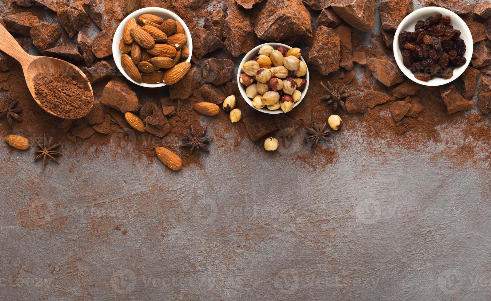 Chocolate chunks on gray background, cocoa powder and variety of nuts and spices bowls, top view. Confectionery shop advertising and cooking ingredients concept, copy space, mockup for recipe photo