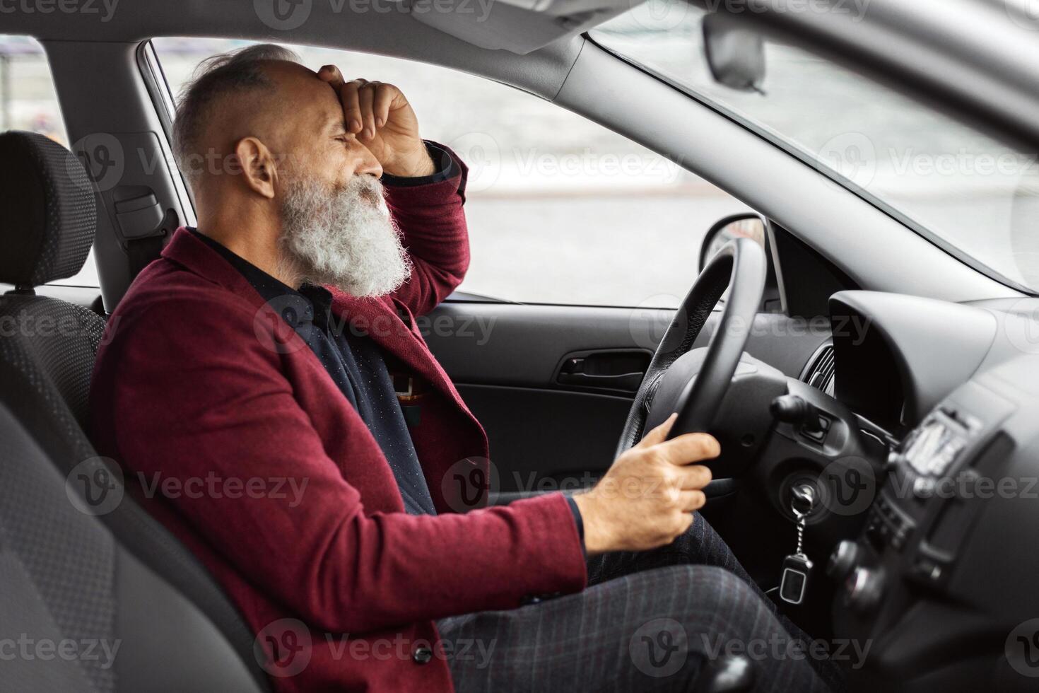 Tired senior businessman having troubles at work, sitting in car, covering his face, side view, copy space. Exhausted grey-haired aged man having headache, suffering from stress at office photo