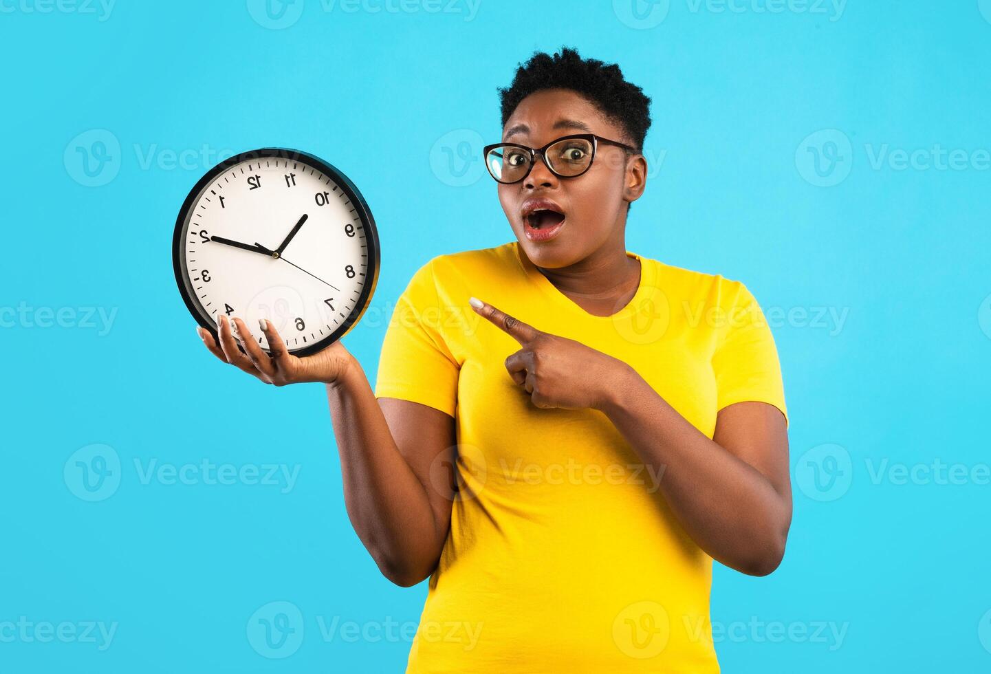 Deadline, Time Is Over. Oversized African Woman Showing Clock Posing Standing Over Blue Studio Background, Looking At Camera. Shocked Black Lady Being Late. Time's Tickling Concept photo