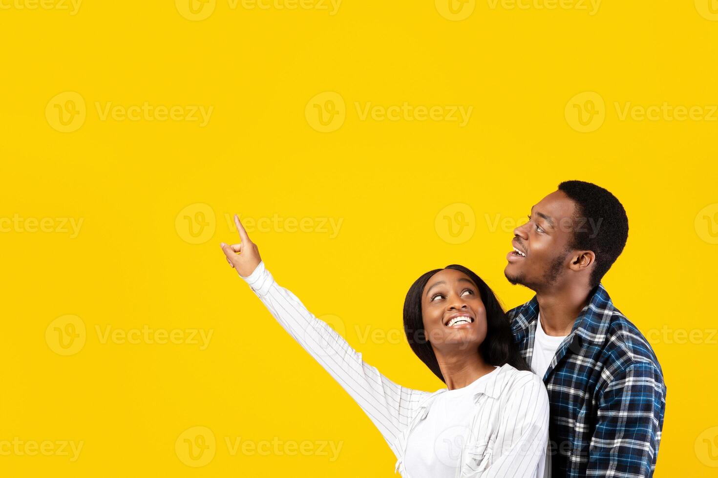 Amazing offer, something unusual and place for advertising or text. Surprised happy zoomers african american male hugs female, lady shows hand up to empty space, isolated on yellow background photo