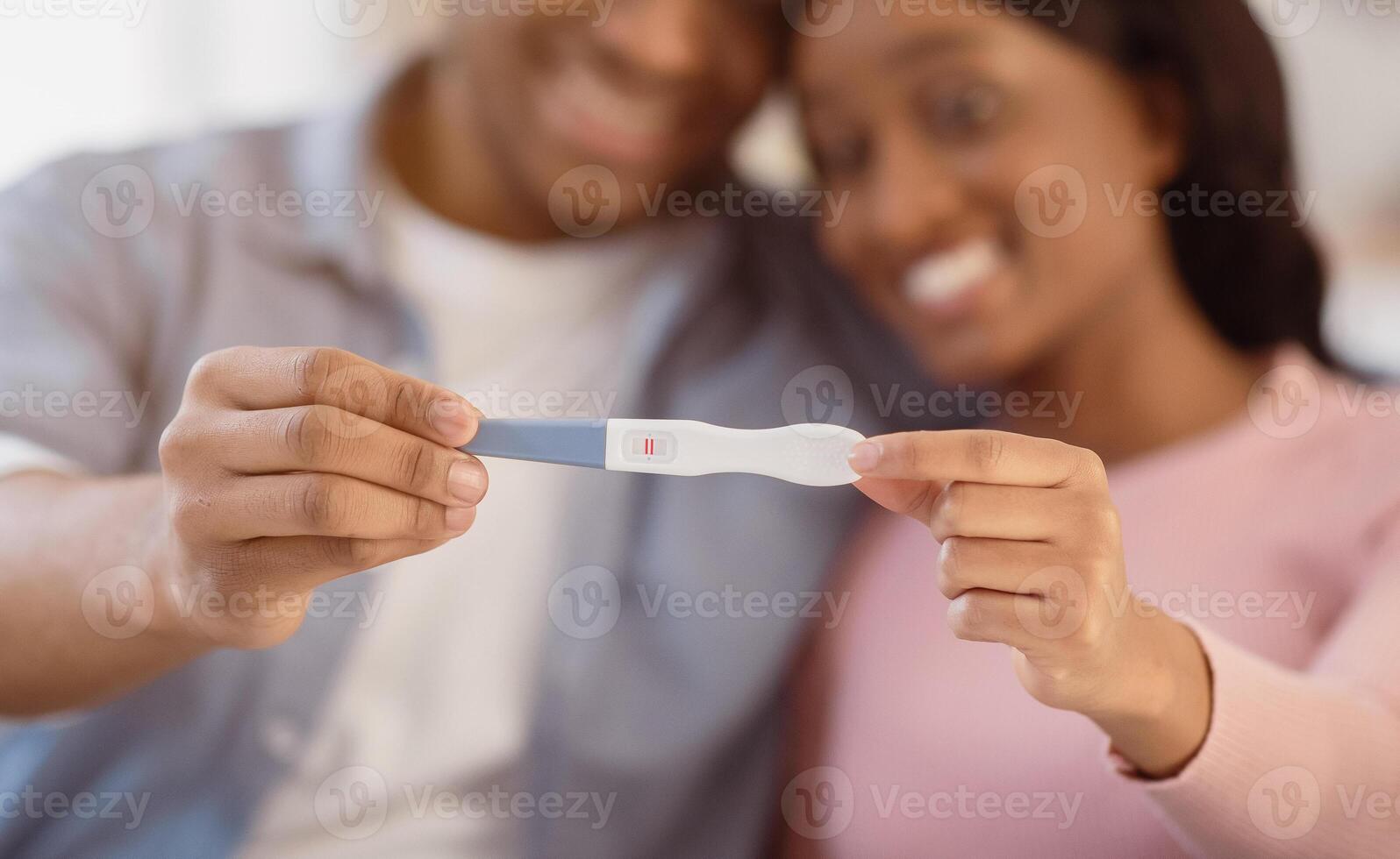 African American married couple showing positive pregnancy test, selective focus. Loving black woman with her husband expecting baby, happy to learn good news. Maternity concept photo