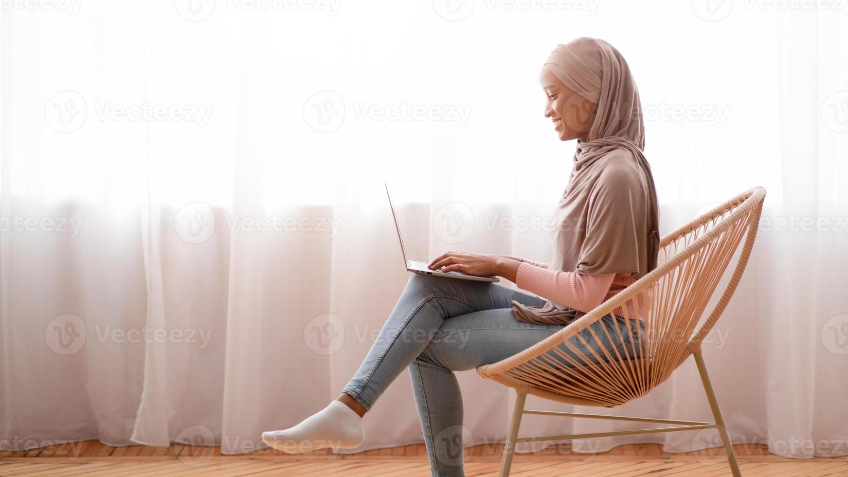 Millennial black Arab lady in traditional hijab using laptop at home, having online conference. African American woman in Muslim headscarf communicating online, taking part in webinar or lecture photo