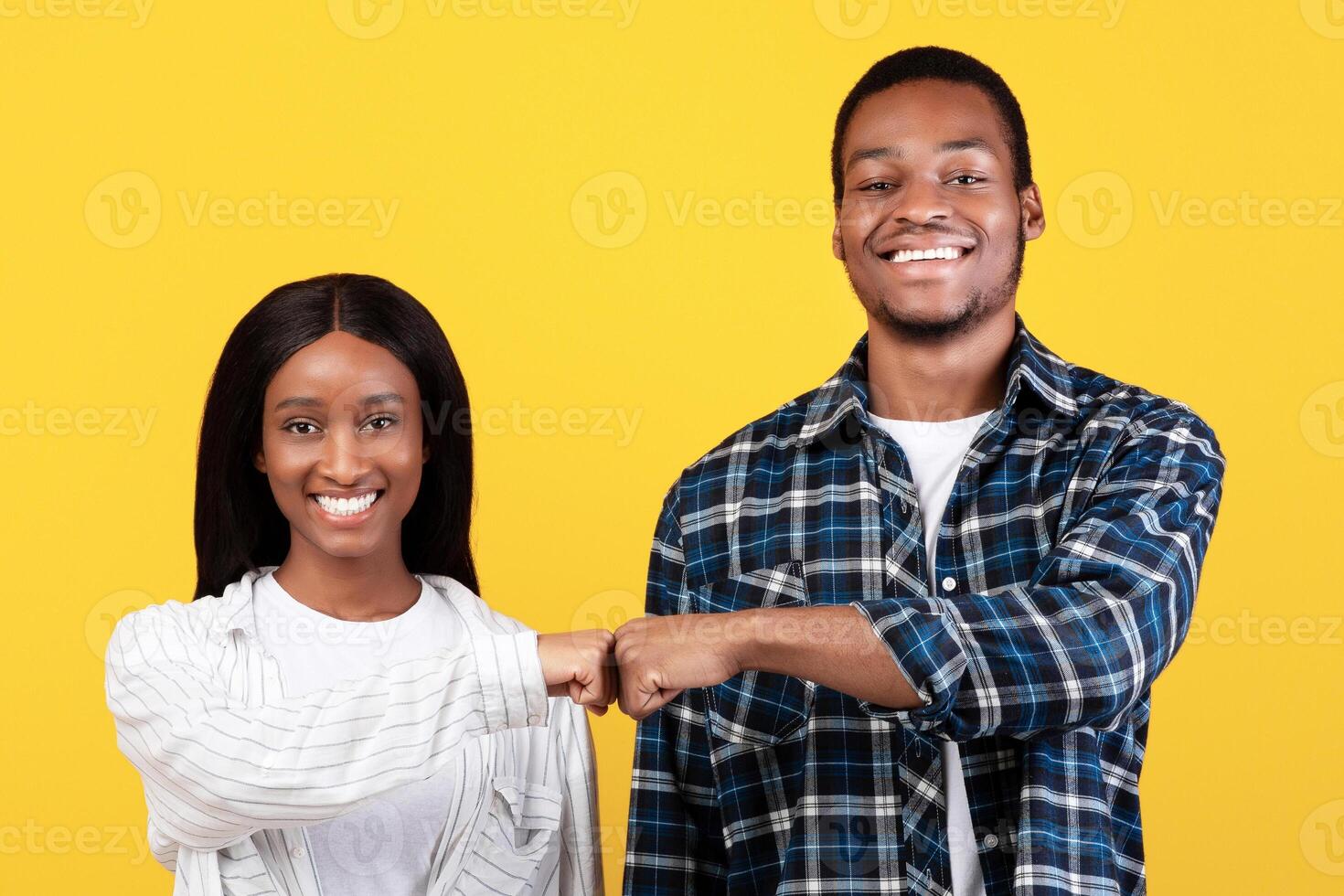 Work as team, agree to do, partnership and collaboration. Young teen happy african american couple give fist bump, agree to bring plan to life, isolated on yellow background, studio shot, free space photo