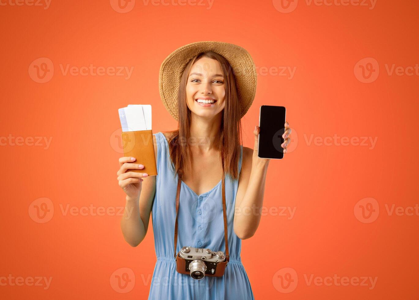 Mobile applications for tourists and travellers. Young woman in summer hat showing mobile phone with empty screen, holding passport and flight tickets, yellow studio background, copy space photo
