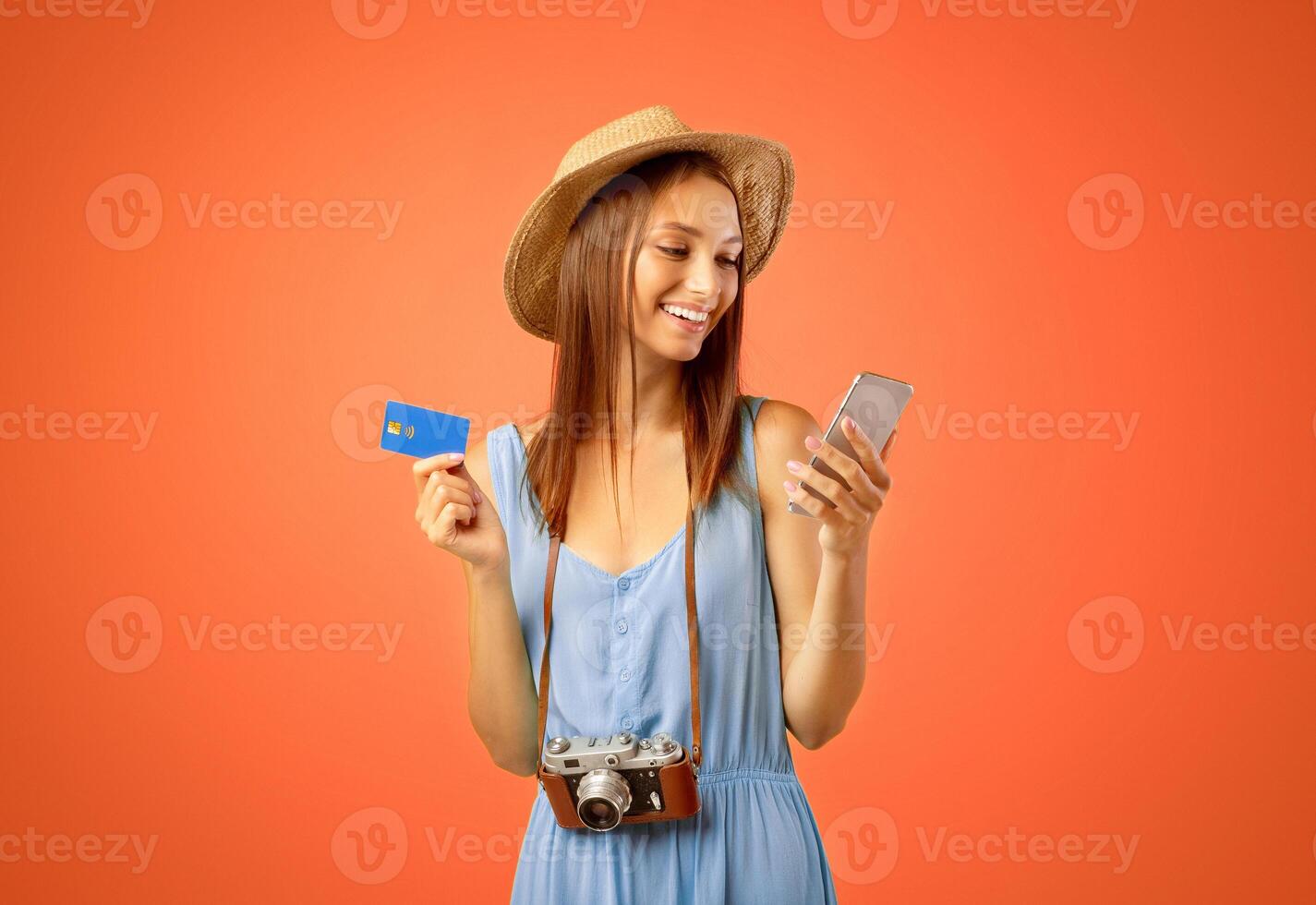 Happy female tourist with smartphone and credit card over yellow studio background, copy space. Cheerful young woman holding credit card and using mobile phone, shopping online while travelling photo
