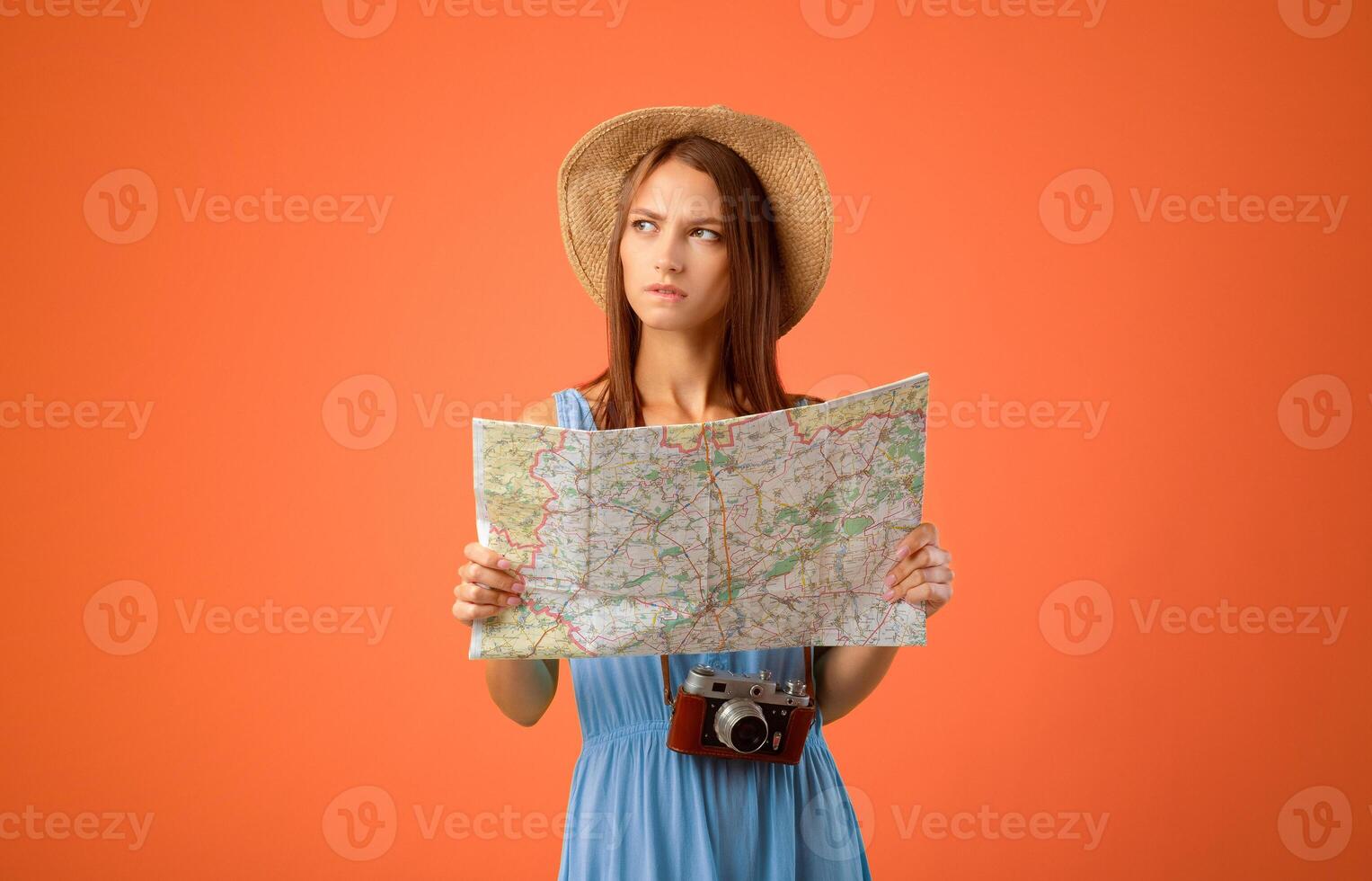 Pensive young woman with camera holding city map and looking at copy space, yellow studio background. Female tourist lady in summer clothes travelling abroad, thinking about place to visit photo