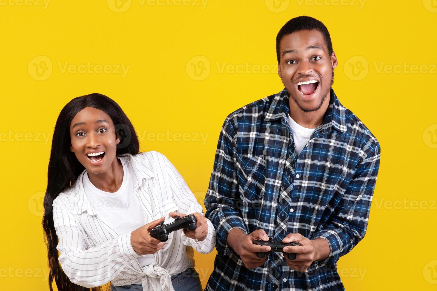 Online games together and entertainment at home. Joyful generation z african american students male and lady playing with gamepads, isolated on yellow background, empty space, studio shot photo