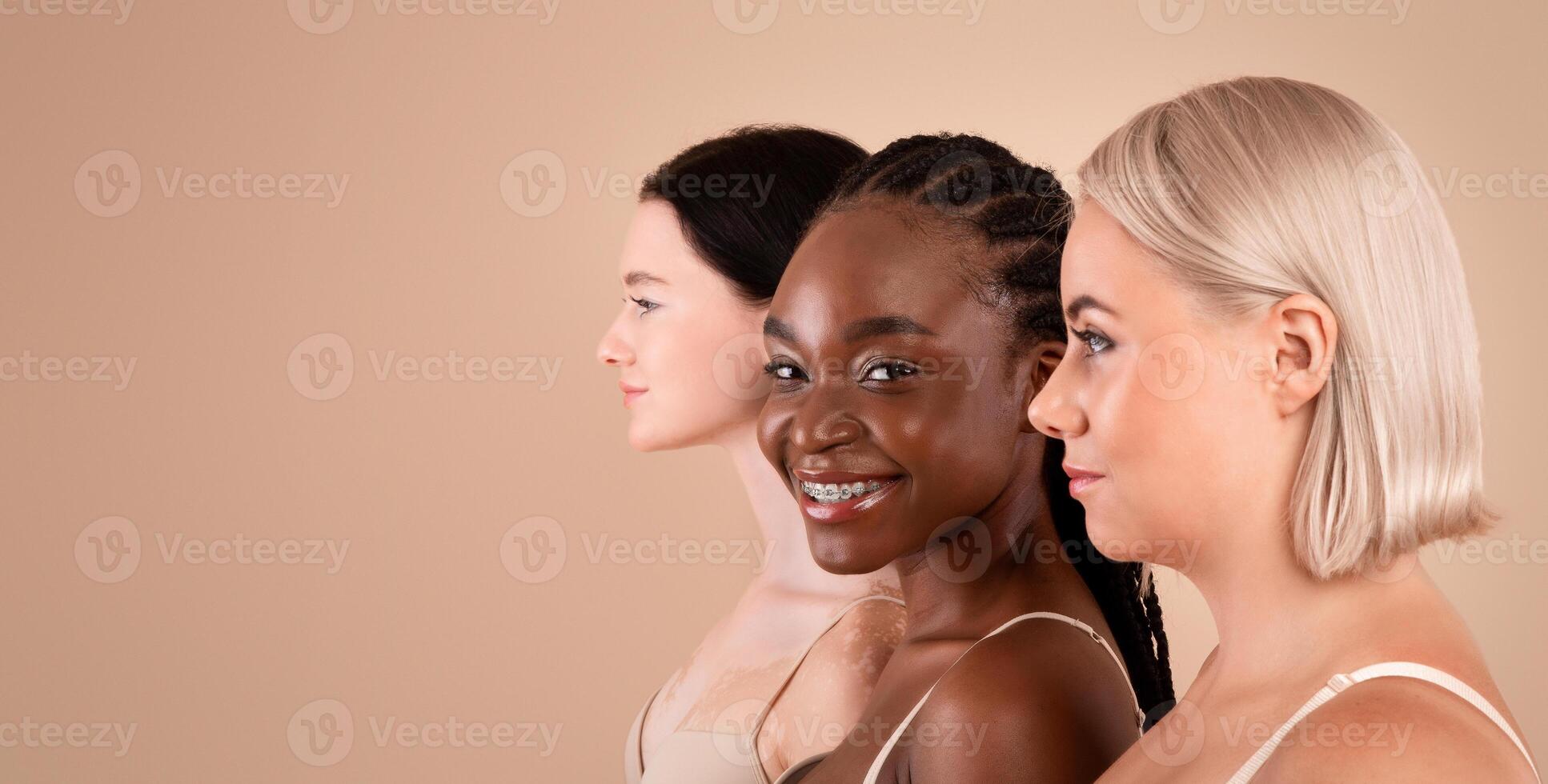 Profile Portrait Of Three Beautiful Body Positive Multiracial Women With Different Appearances Posing In Bra's Over Beige Background, Young African American Female Smiling At Camera, Copy Space photo