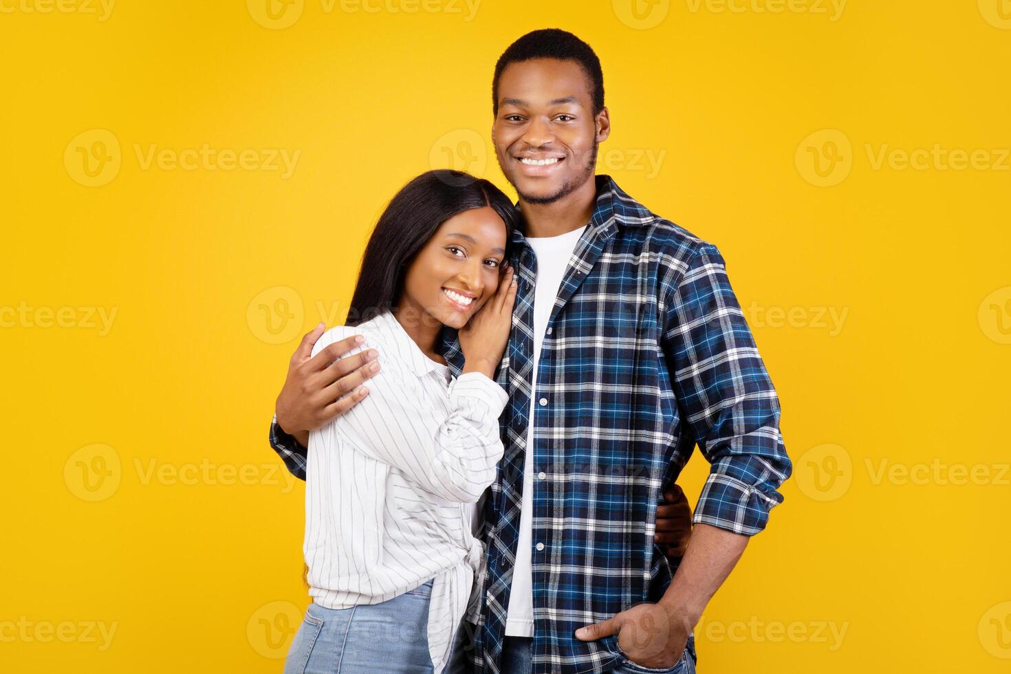 Natural human emotions of couple in love. Portrait of happy young african american man and woman in casual hugging and looking at camera isolated on yellow background, studio shot, free space photo