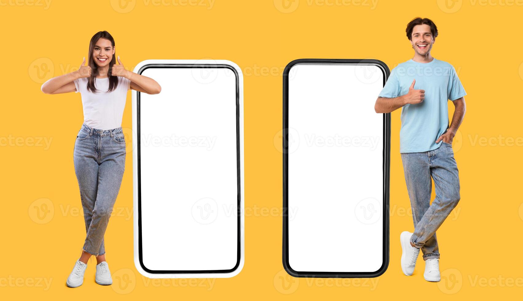 We Like This App. Full body length of happy couple standing next to 2 smart phones with white empty screen for mock up, young lady and guy showing thumb up sign gesture, panorama, banner, free space photo