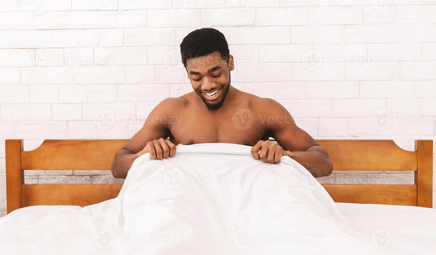 Excited african-american guy looking at his strong morning erection under sheets and smiling, panorama photo