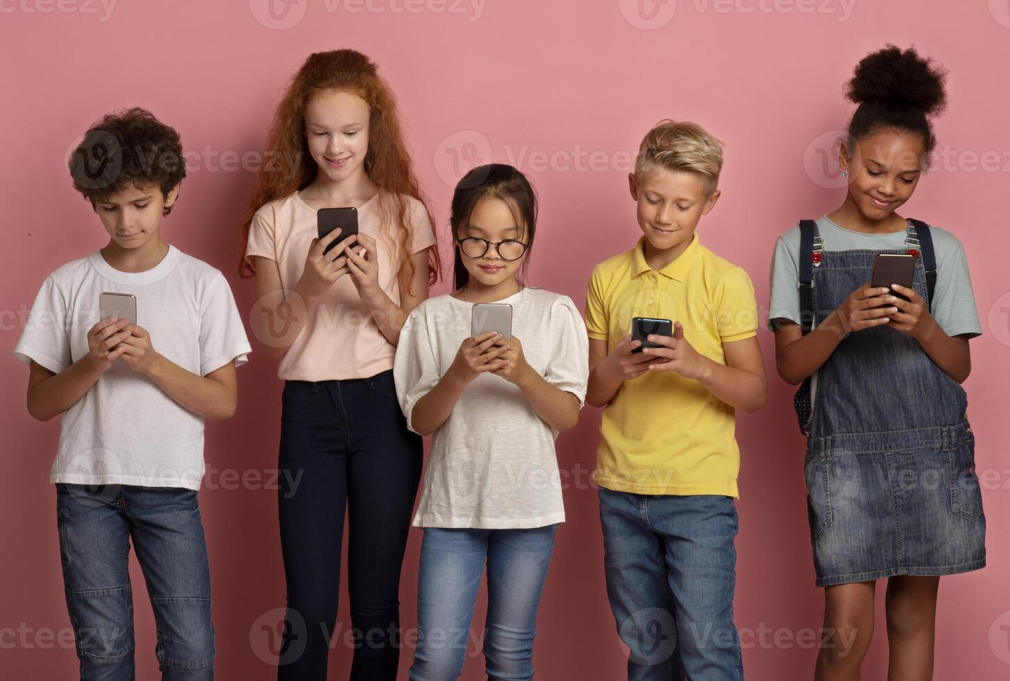 Group of diverse schoolkids stuck in mobile phones studying online over pink background photo