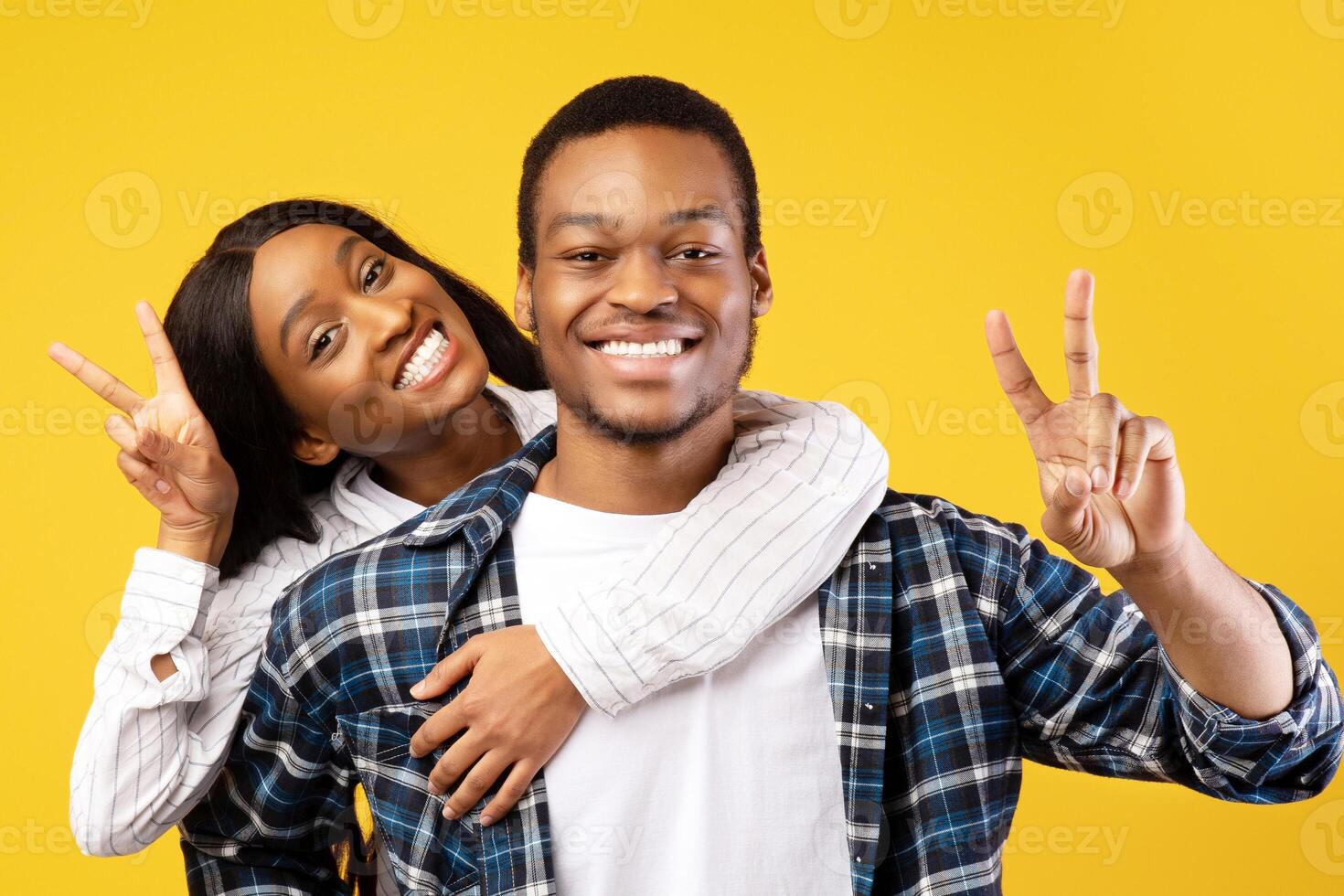 Freedom, vacation, free time and funny of millennials. Smiling young african american guy and holds female on back and show sign of peace, isolated on yellow background, studio shot, copy space photo