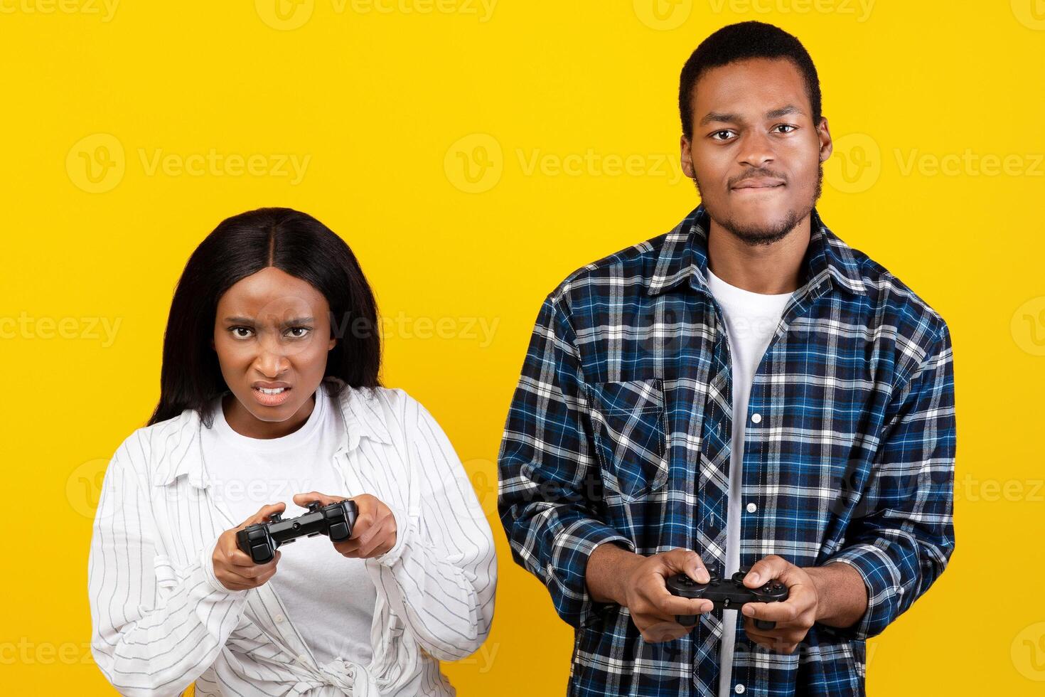 Online battle, free time and relationships. Tense excited homelander's african american man and woman with gamepads in hands playing in game, isolated on yellow background, studio shot, free space photo