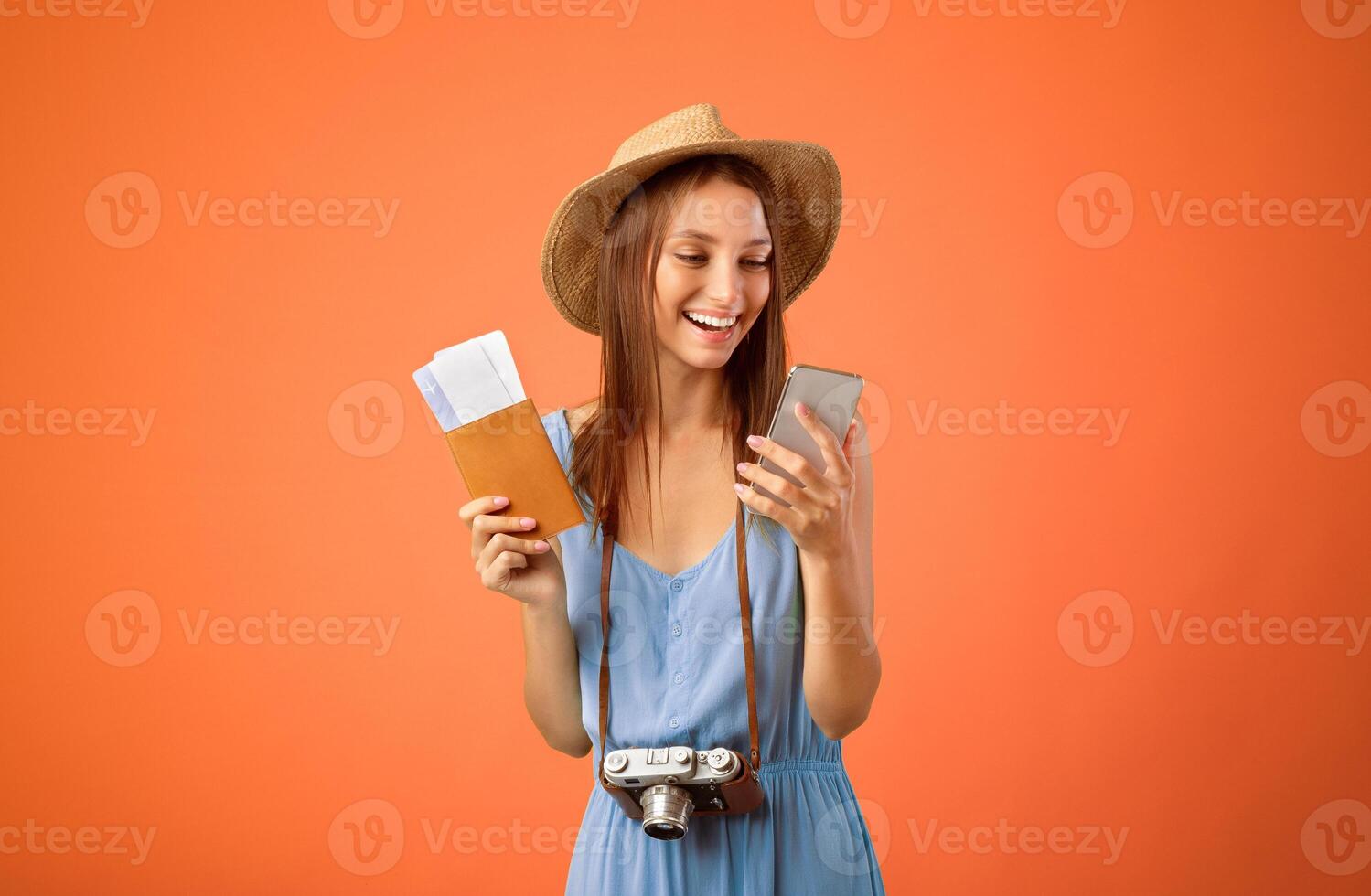 Mobile applications for tourists and travellers. Happy young woman in summer hat using mobile phone, holding passport and flight tickets, posting on social media, yellow studio background, copy space photo