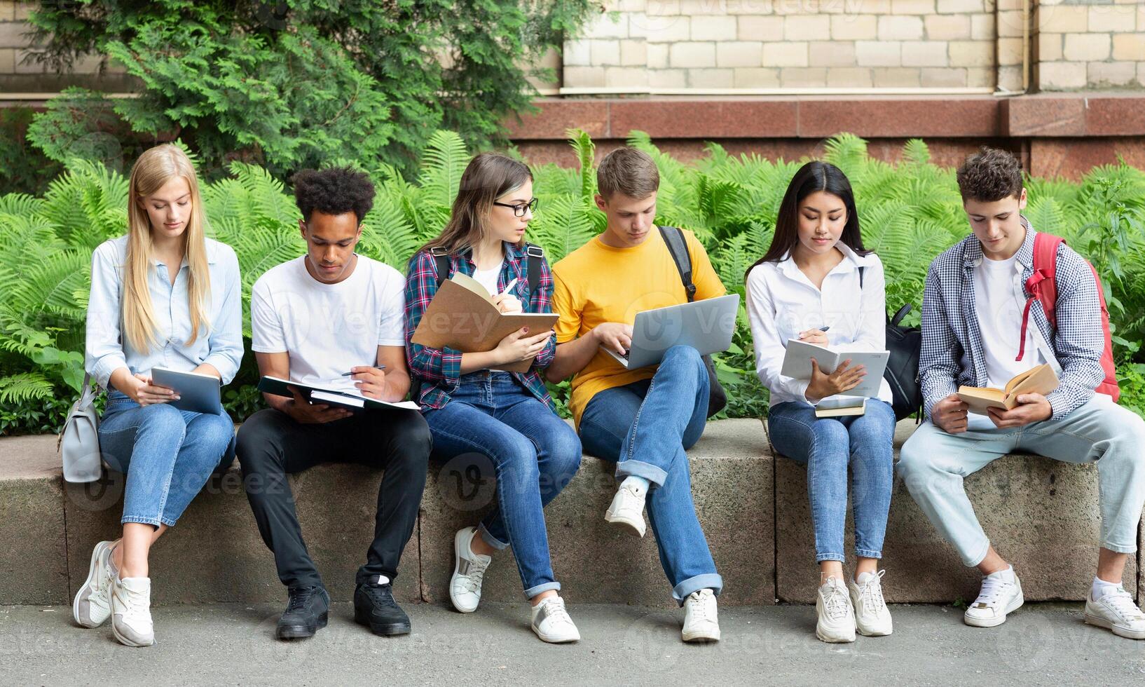 Students preparing for lecture. Teens sitting in university campus with books and devices photo