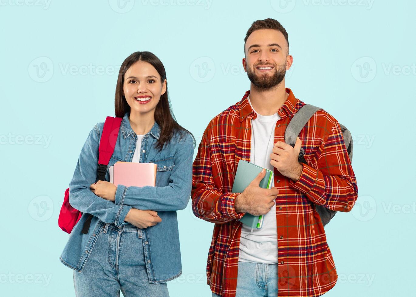 Modern Students. Cheerful Young Guy And Lady Holding Books Posing With Their Backpacks, Smiling To Camera On Blue Background. Young Couple Of Learners Standing Together Ready For College Study photo