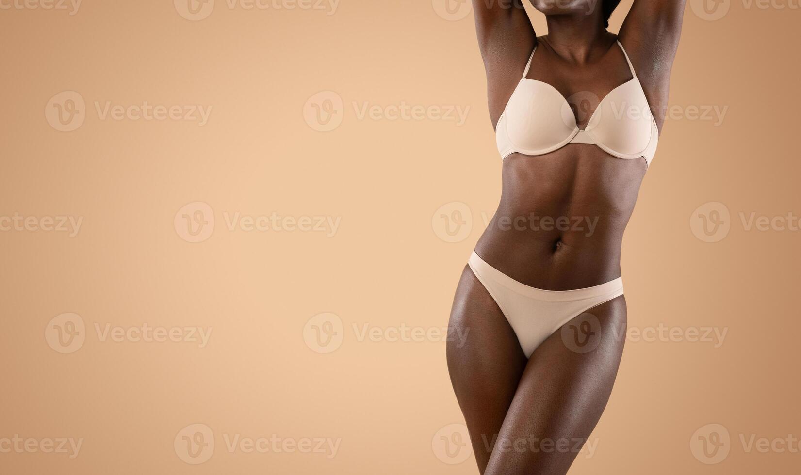 Attractive slender black lady with hands up posing in underwear over beige studio background, showing her beautiful curves, cropped, panorama with copy space. Diet, athletic body concept photo