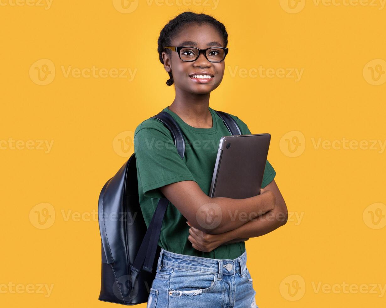 Smiling African Female Student Holding Laptop Hugging Computer Posing Standing On Yellow Studio Background. E-Learning And Educational Gadgets, Distant Online Study And Student's Lifestyle Concept photo