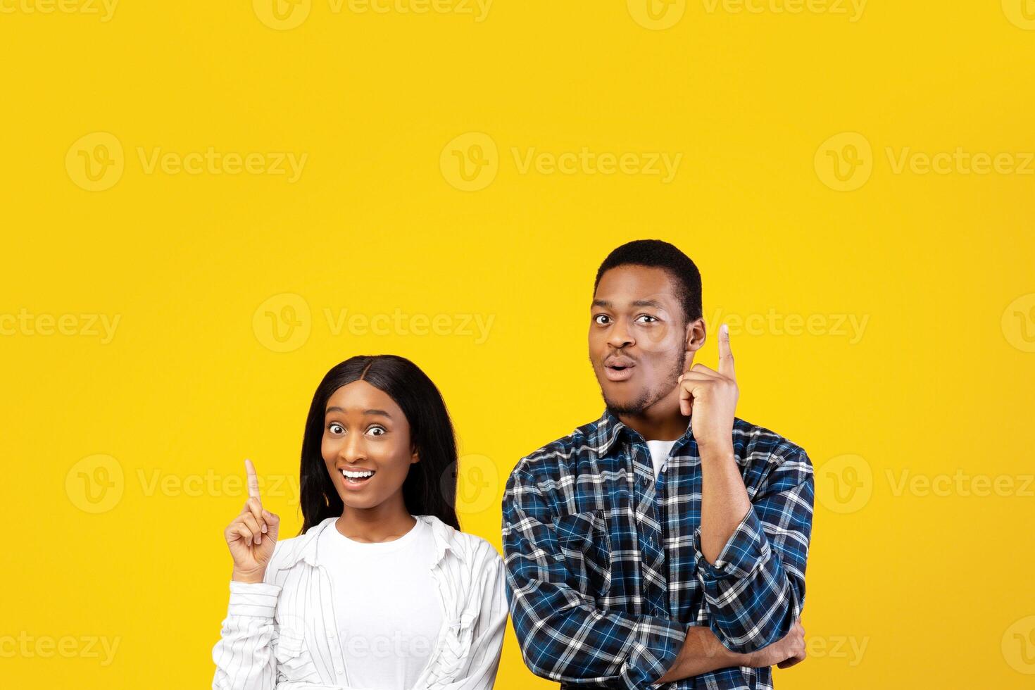 Got an idea, solution and facial emotions of people. Excited joyful young african american couple point fingers up, making decision, isolated on yellow background, studio shot, square, free space photo